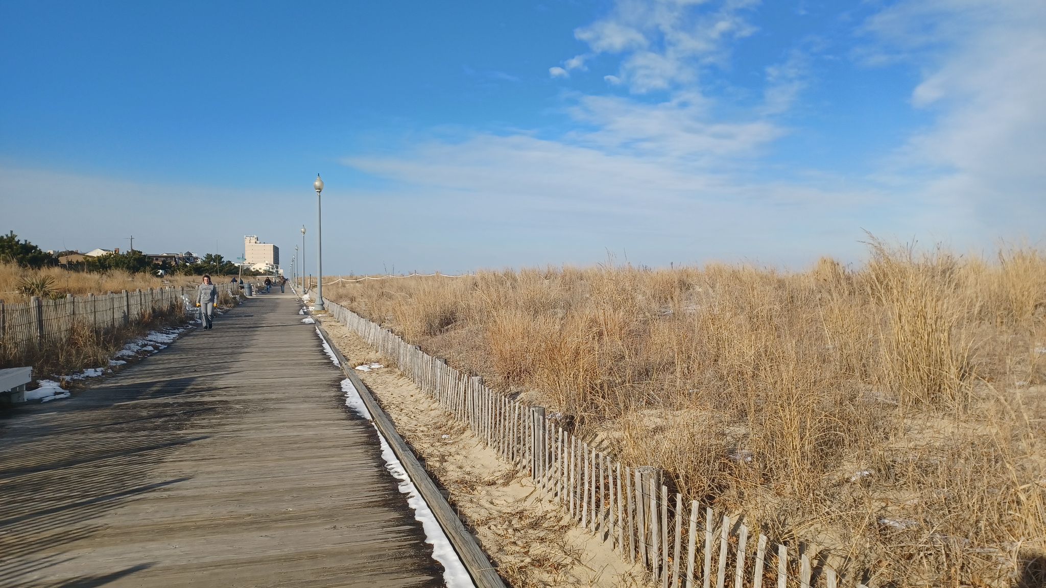 Boardwalk alongside dry dune grass and fence under a bright blue sky. - Rehoboth Beach Boardwalk