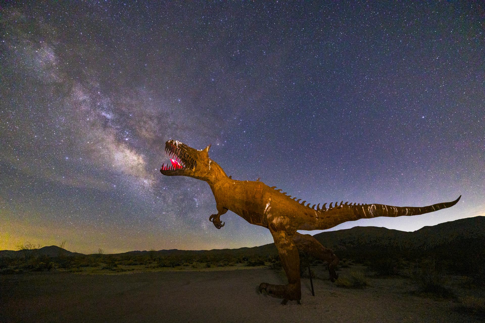 Dinosaur sculpture under a breathtaking starry night sky with the Milky Way.