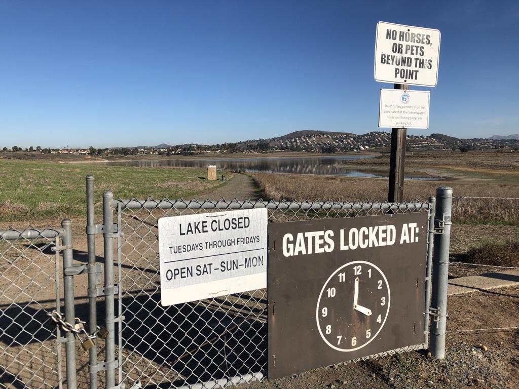 A chain-link gate with signs about lake access and closing times.