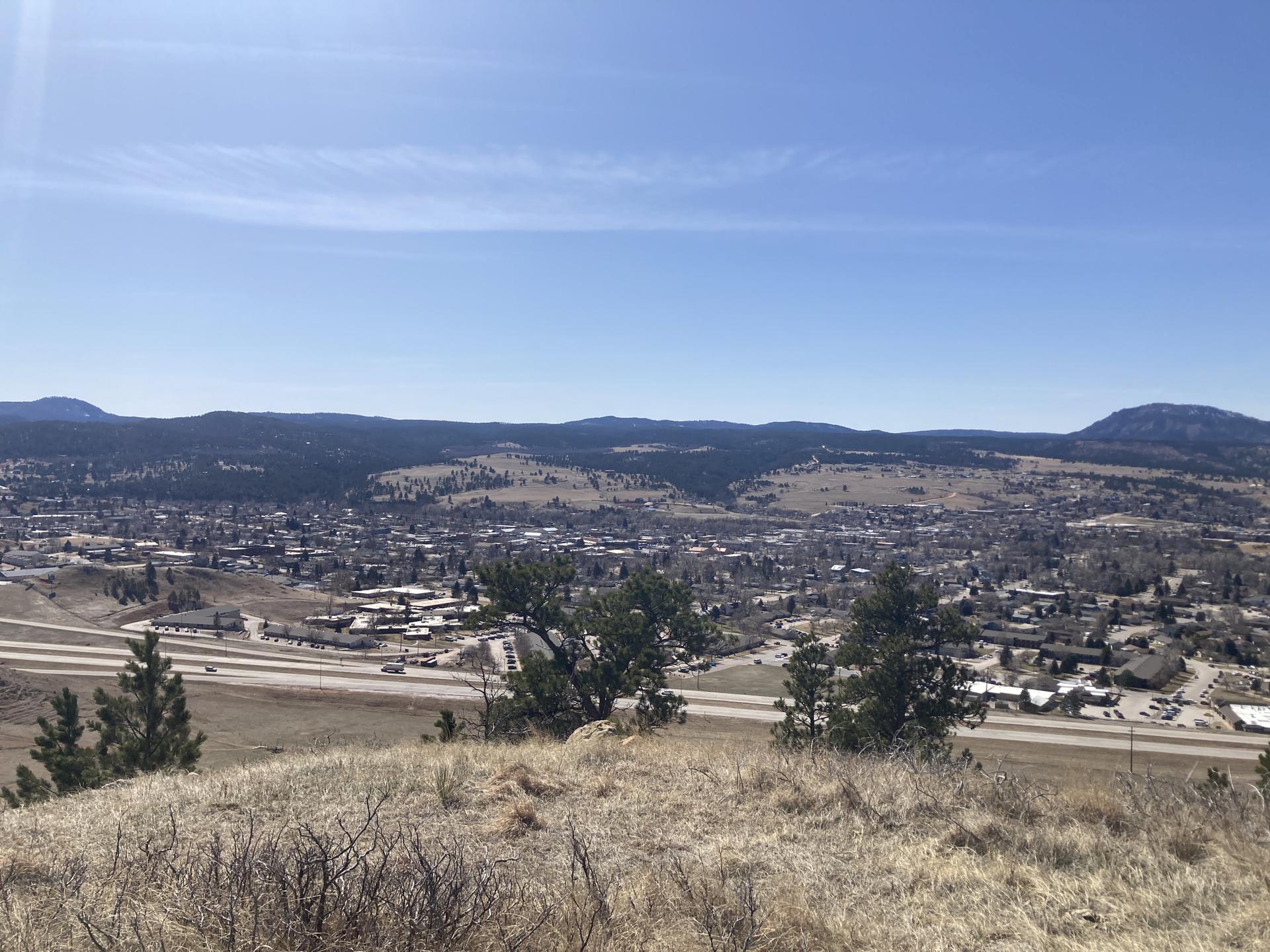 Sunny panoramic view of a town in a valley with mountains and dry grass.