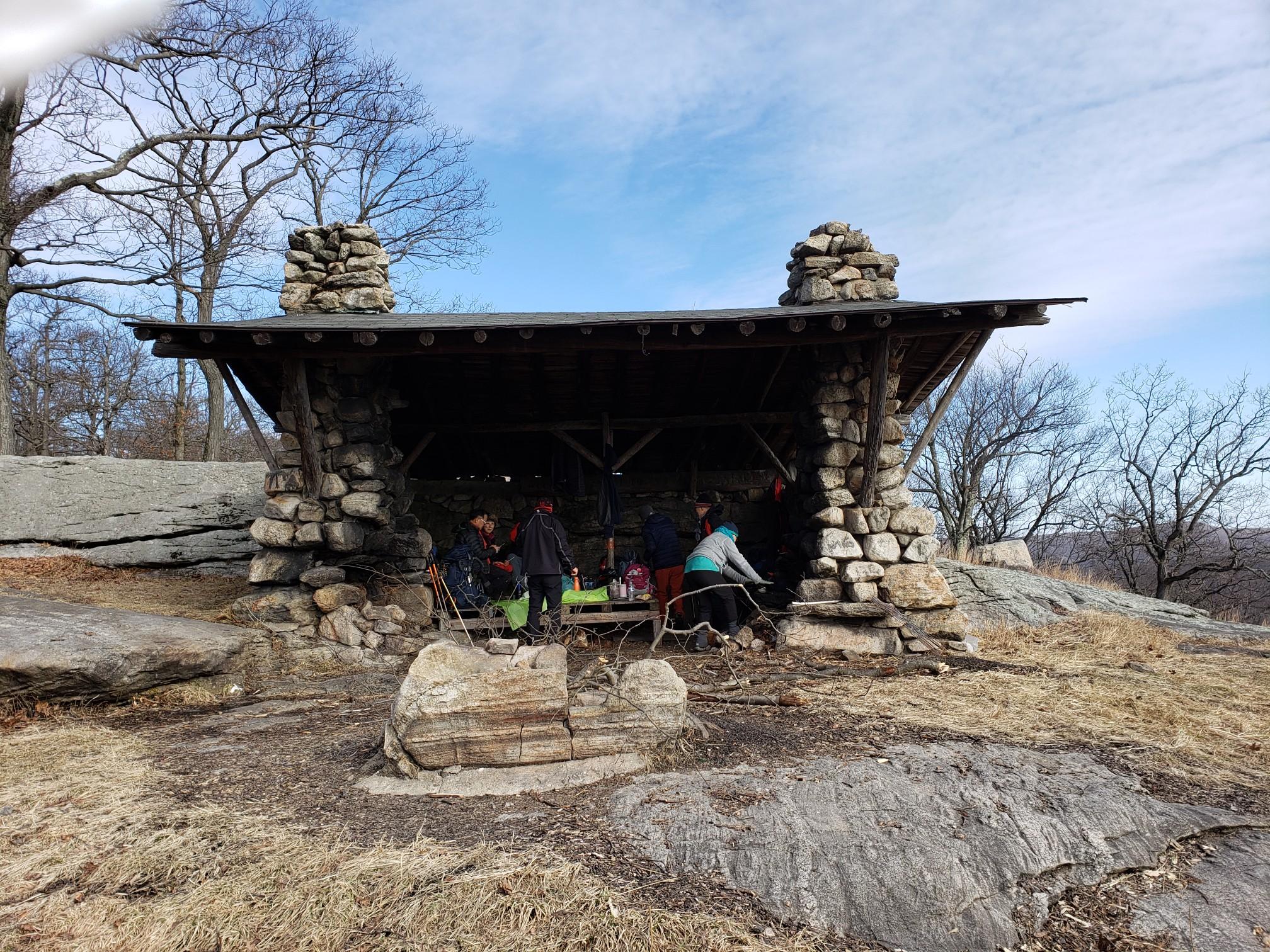 People gathered inside a rustic stone and wood shelter on a rocky hillside.