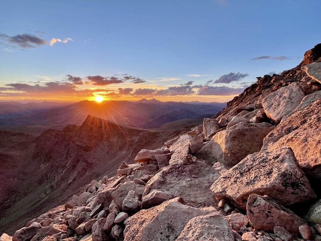 Golden sunset over a vast mountain range with large rocks in the foreground.