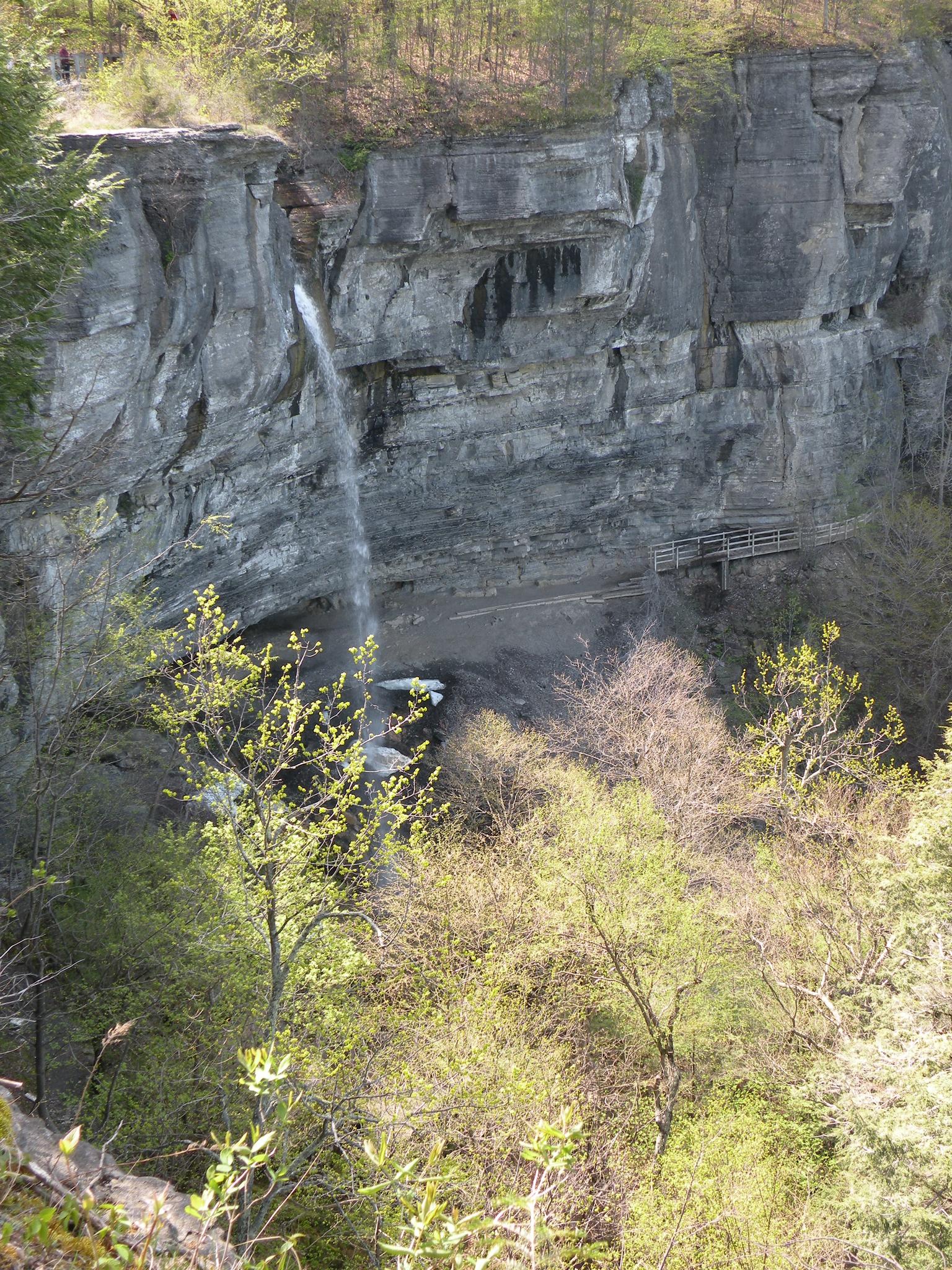 Sunny view of a waterfall plunging down a tall, grey cliff.