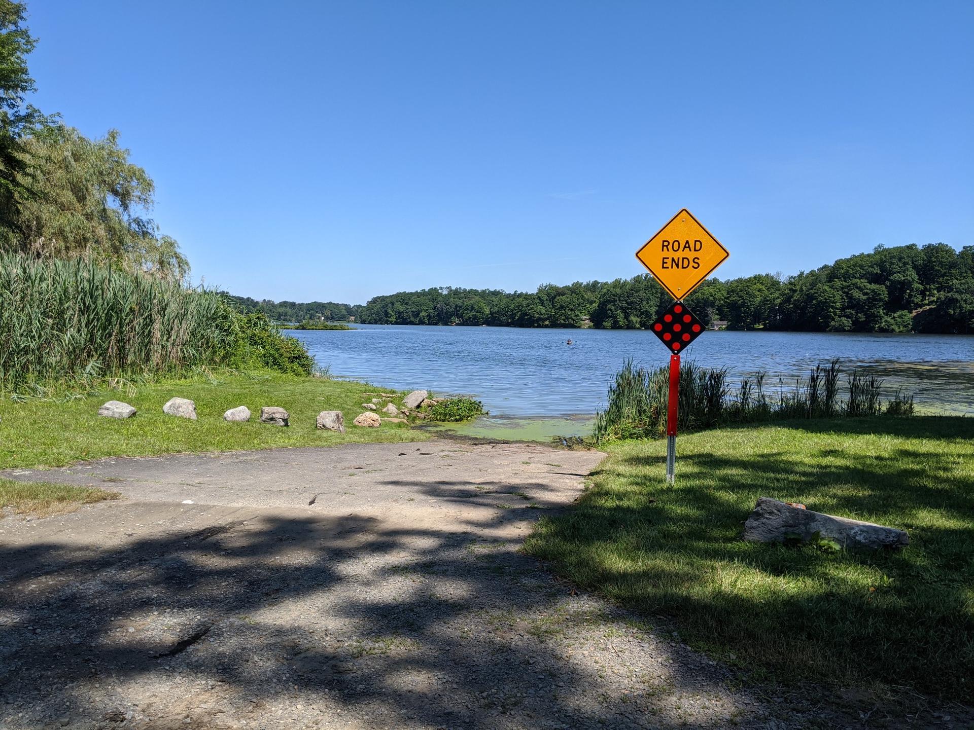 A boat ramp and "Road Ends" sign by a sunny lake.
