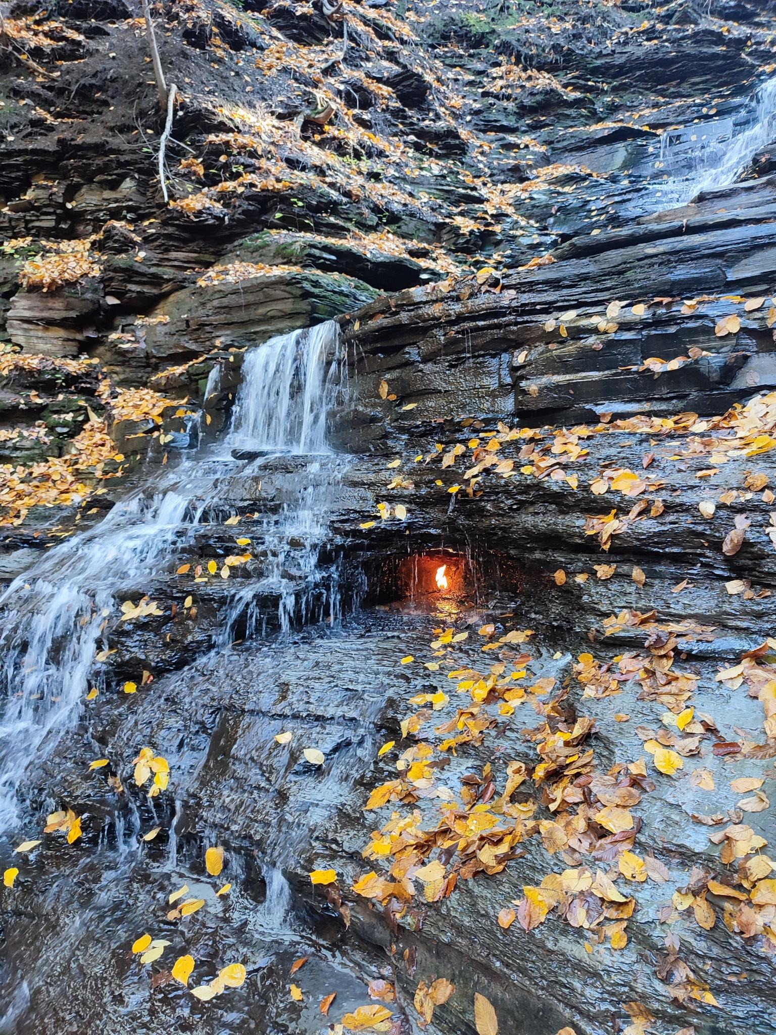 Waterfall cascading over rocky ledges with autumn leaves and a glowing light.