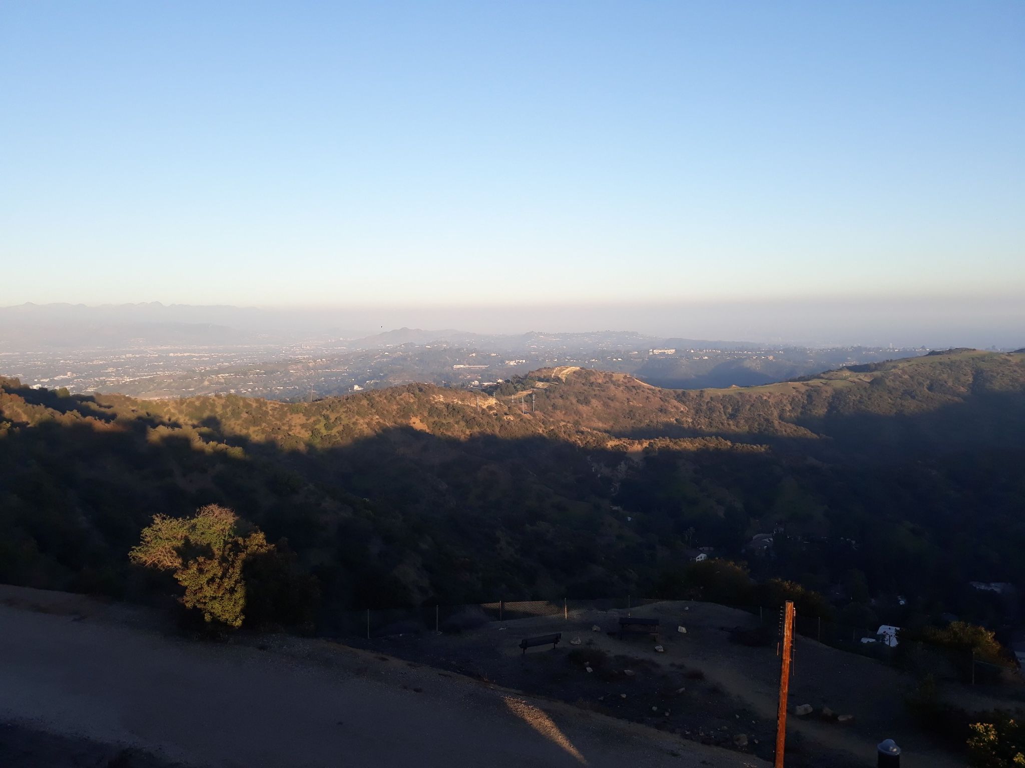 Hazy panoramic view of rolling hills and a distant city at sunset. - San Vicente Mountain Viewpoint – West Mandeville Fire Road loop from Downtown Santa Monica