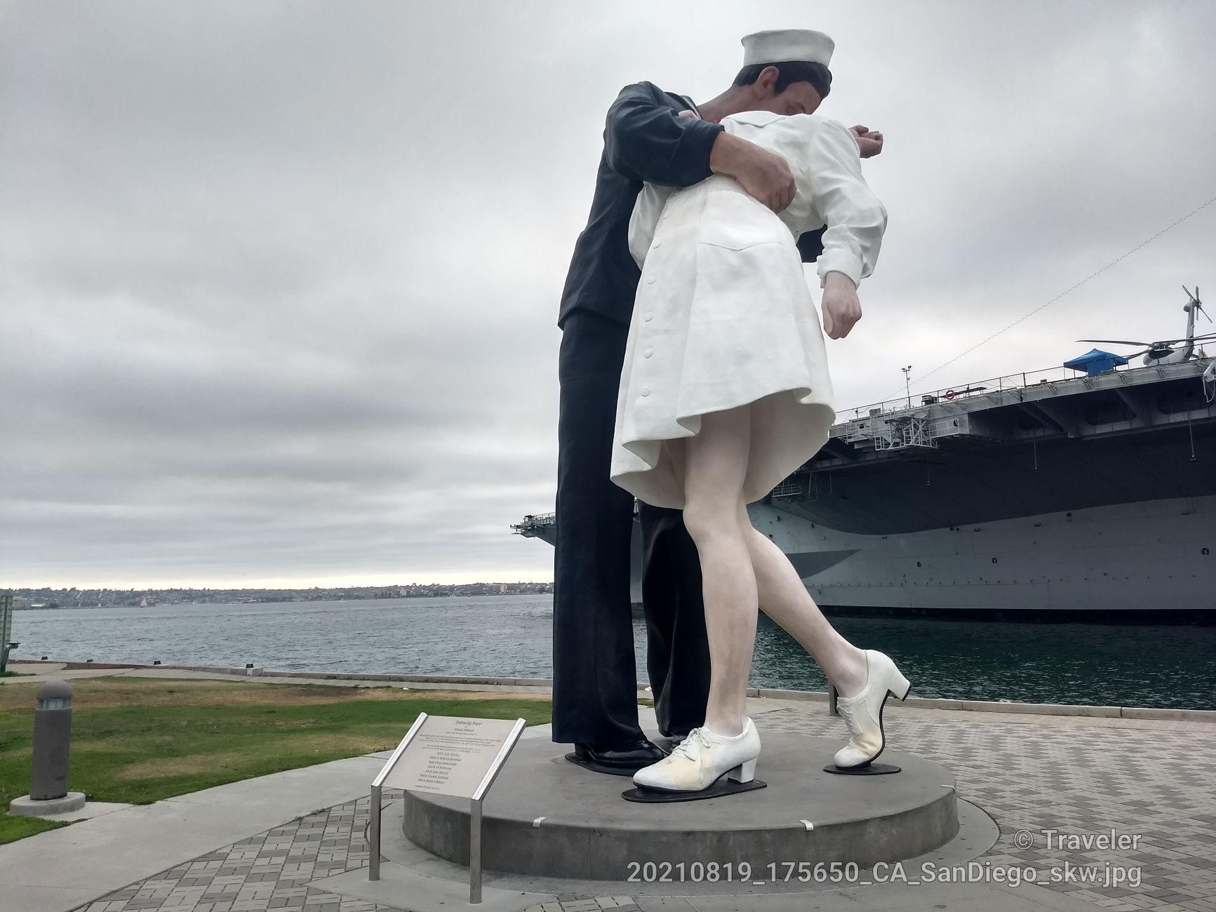 Large statue of a sailor kissing a nurse by the water, ship behind.