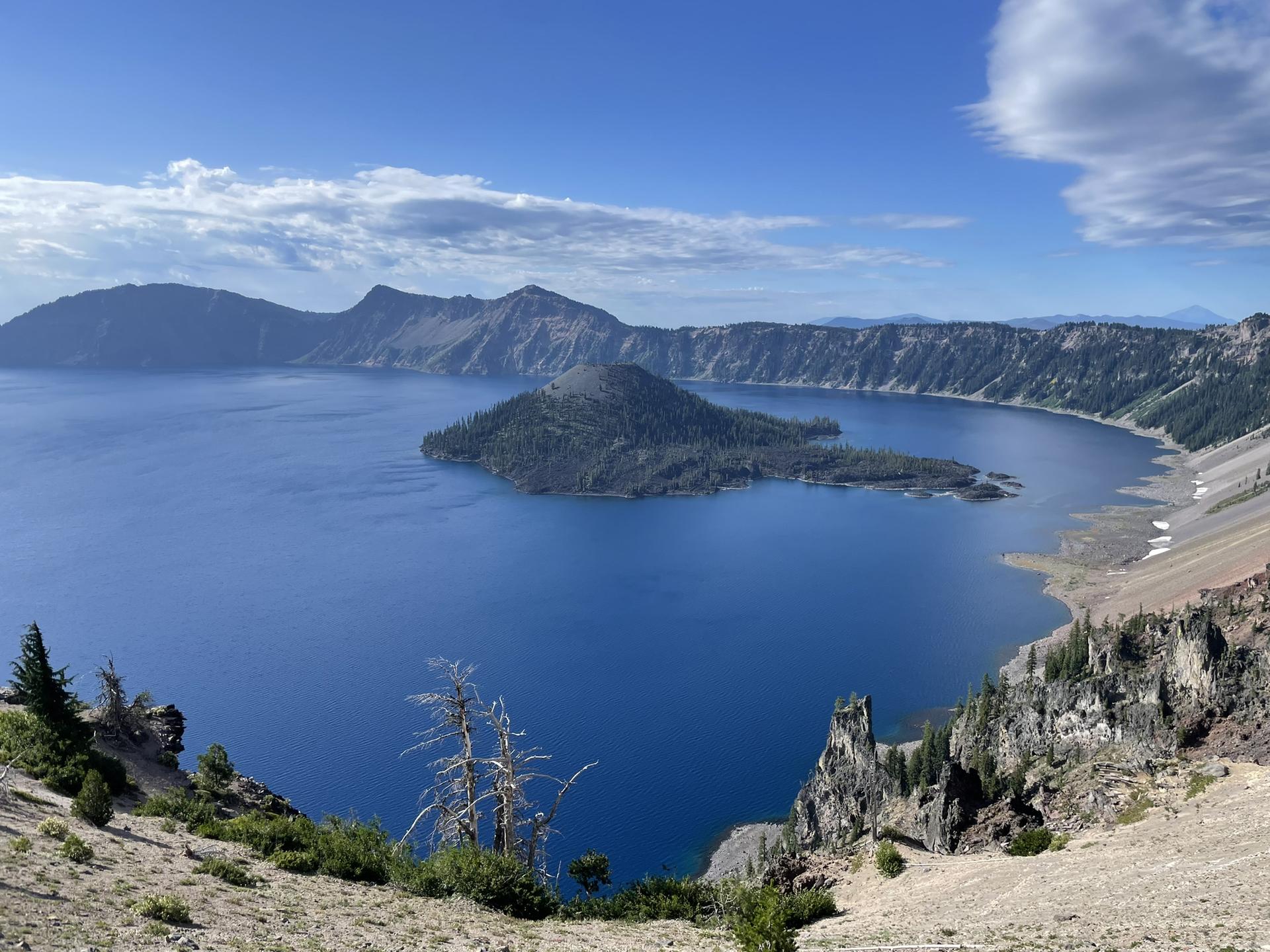 Expansive blue lake with a central island, surrounded by rugged mountains under a bright sky.