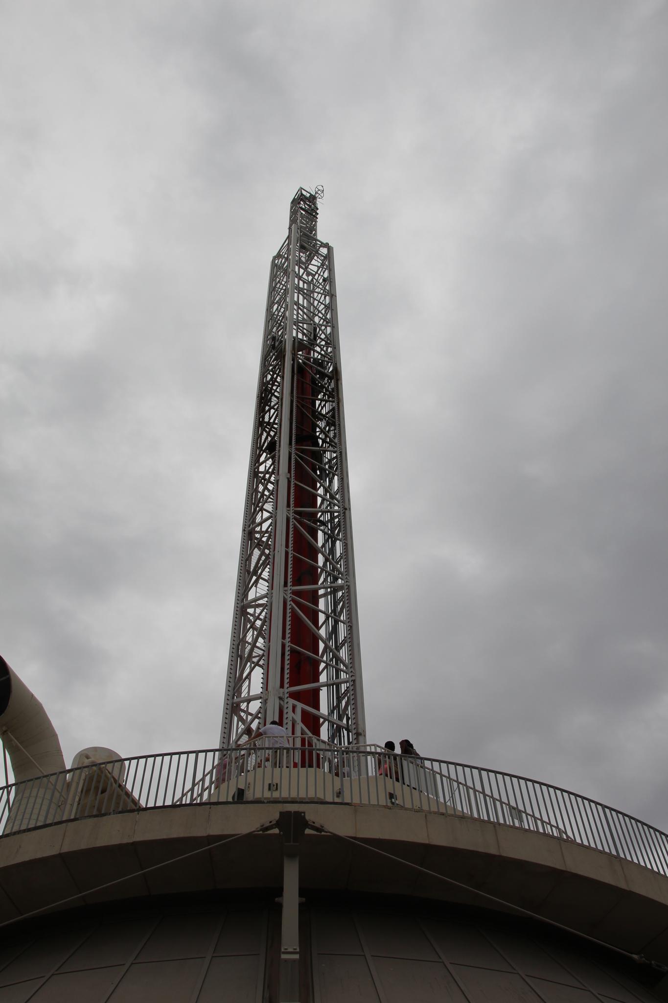 A tall metal tower rises from a building under a cloudy sky.