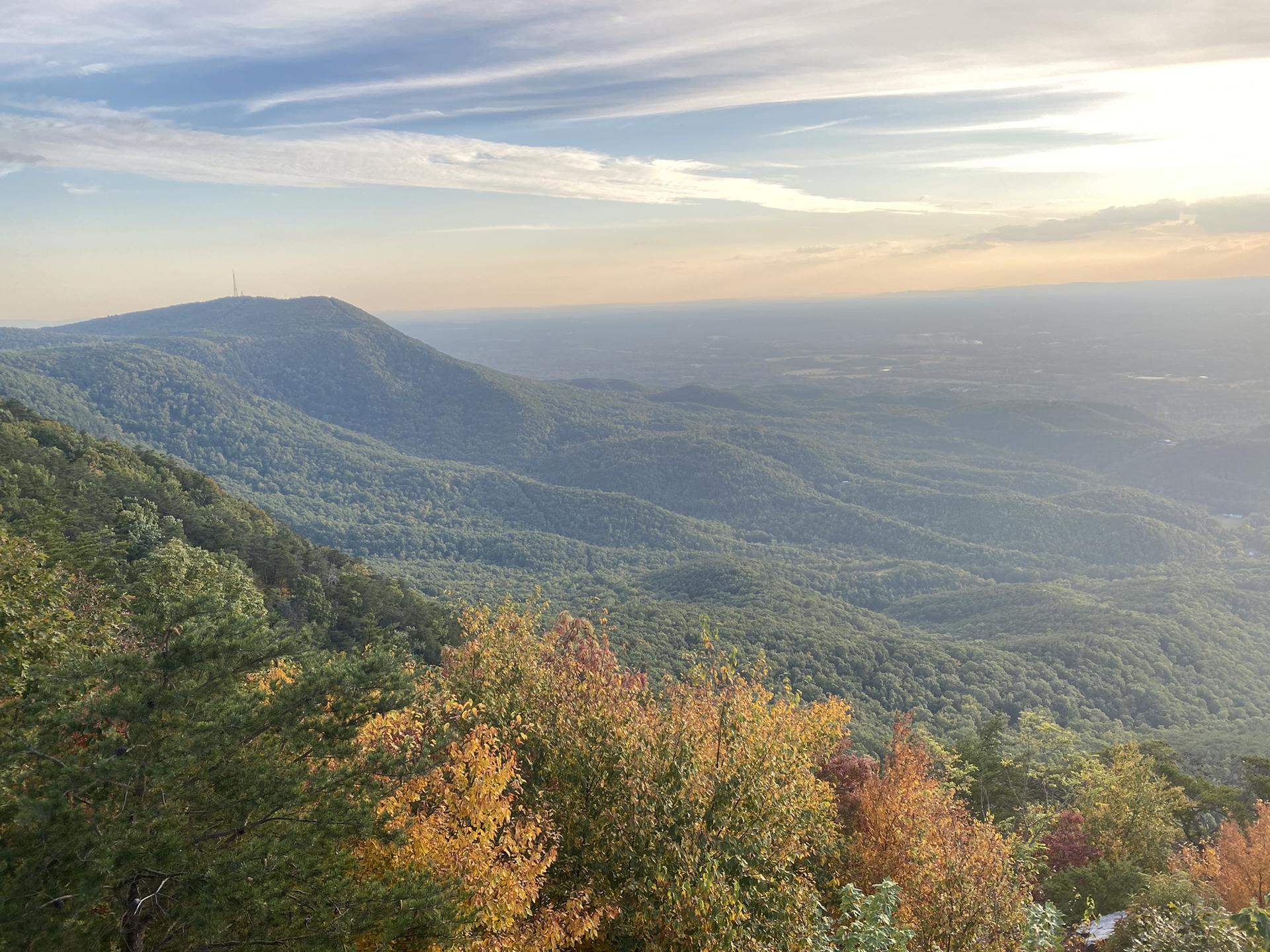 Hazy mountain vista with colorful autumn trees under a soft, cloudy sky.