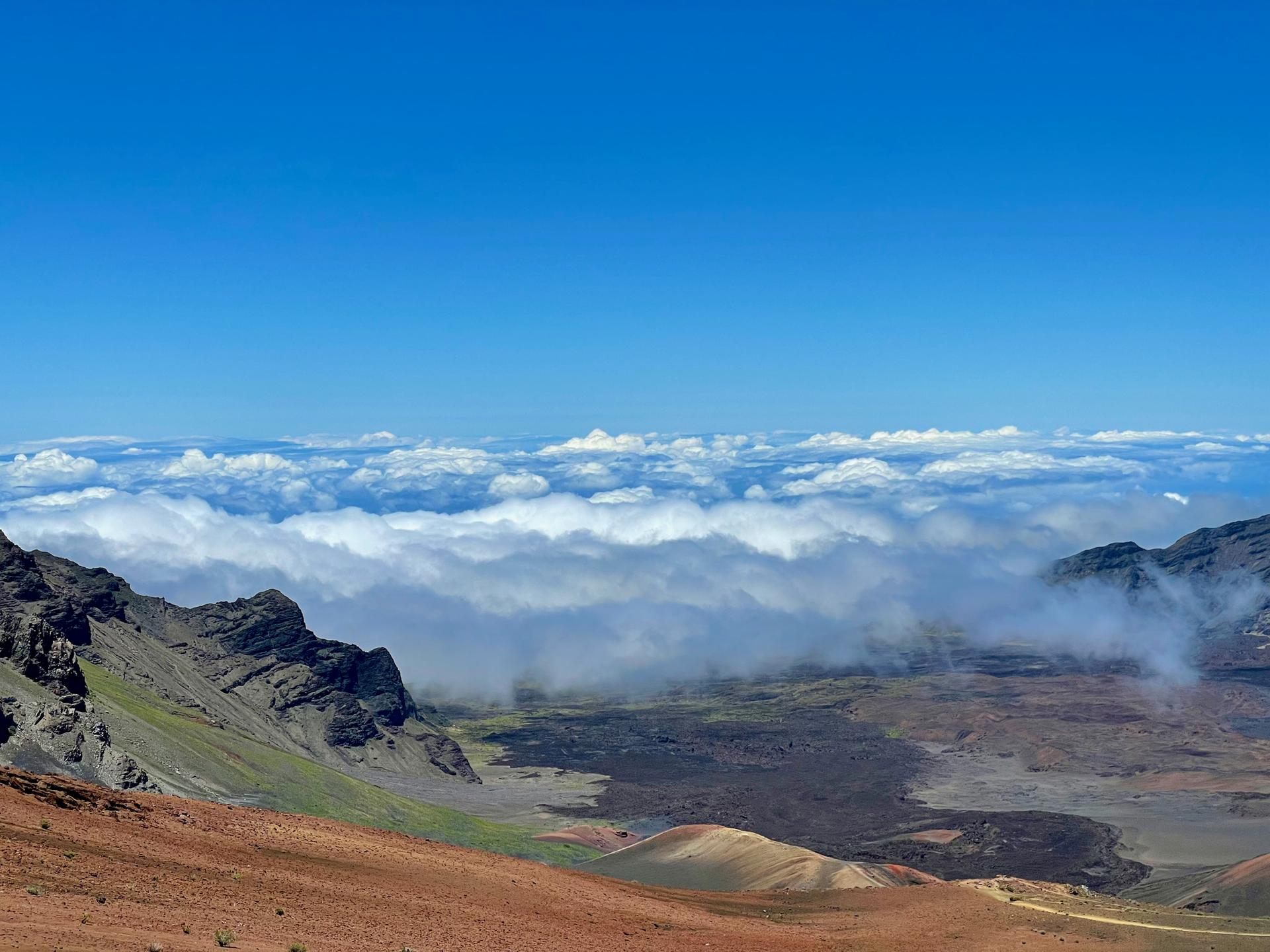 Panoramic view of clouds filling a mountain valley under a blue sky.
