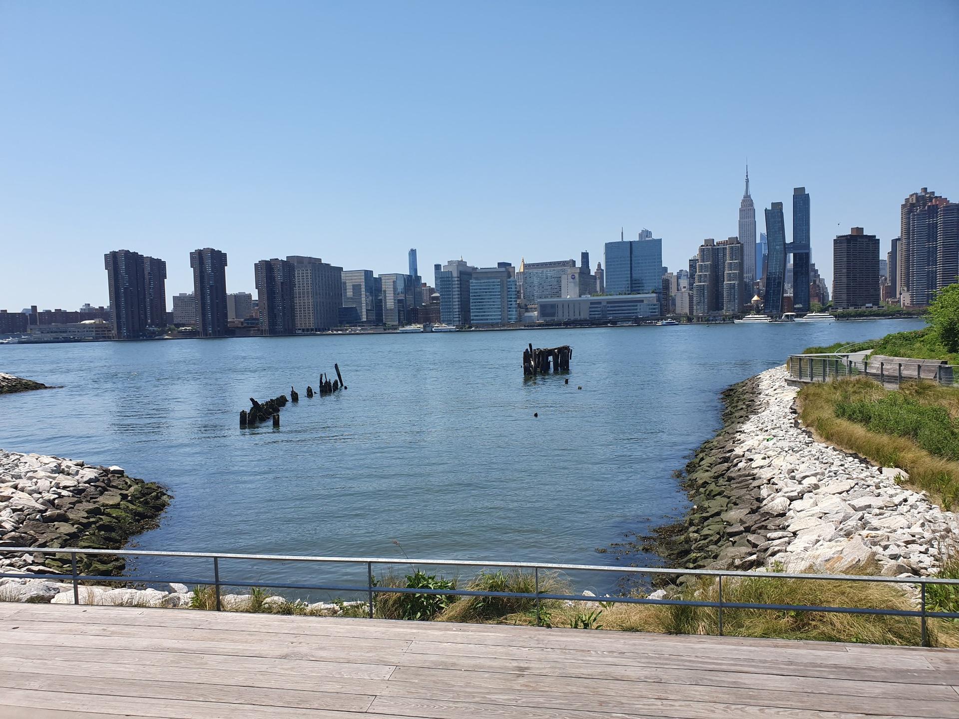 Sunny waterfront view of a city skyline across a wide river.
