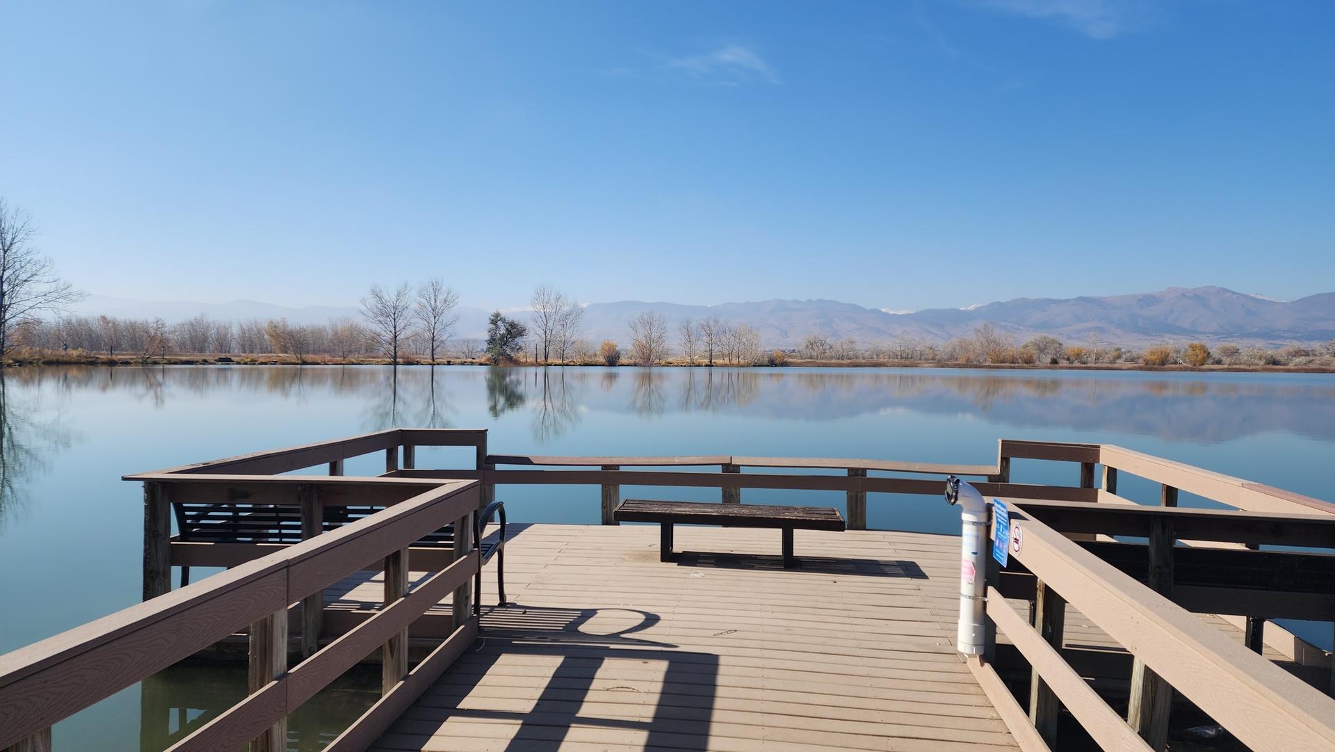 Wooden pier on a calm lake with distant mountains under a clear blue sky.