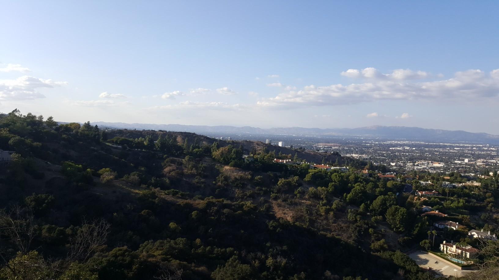 Panoramic view of a sprawling city nestled among hills under a bright blue sky.