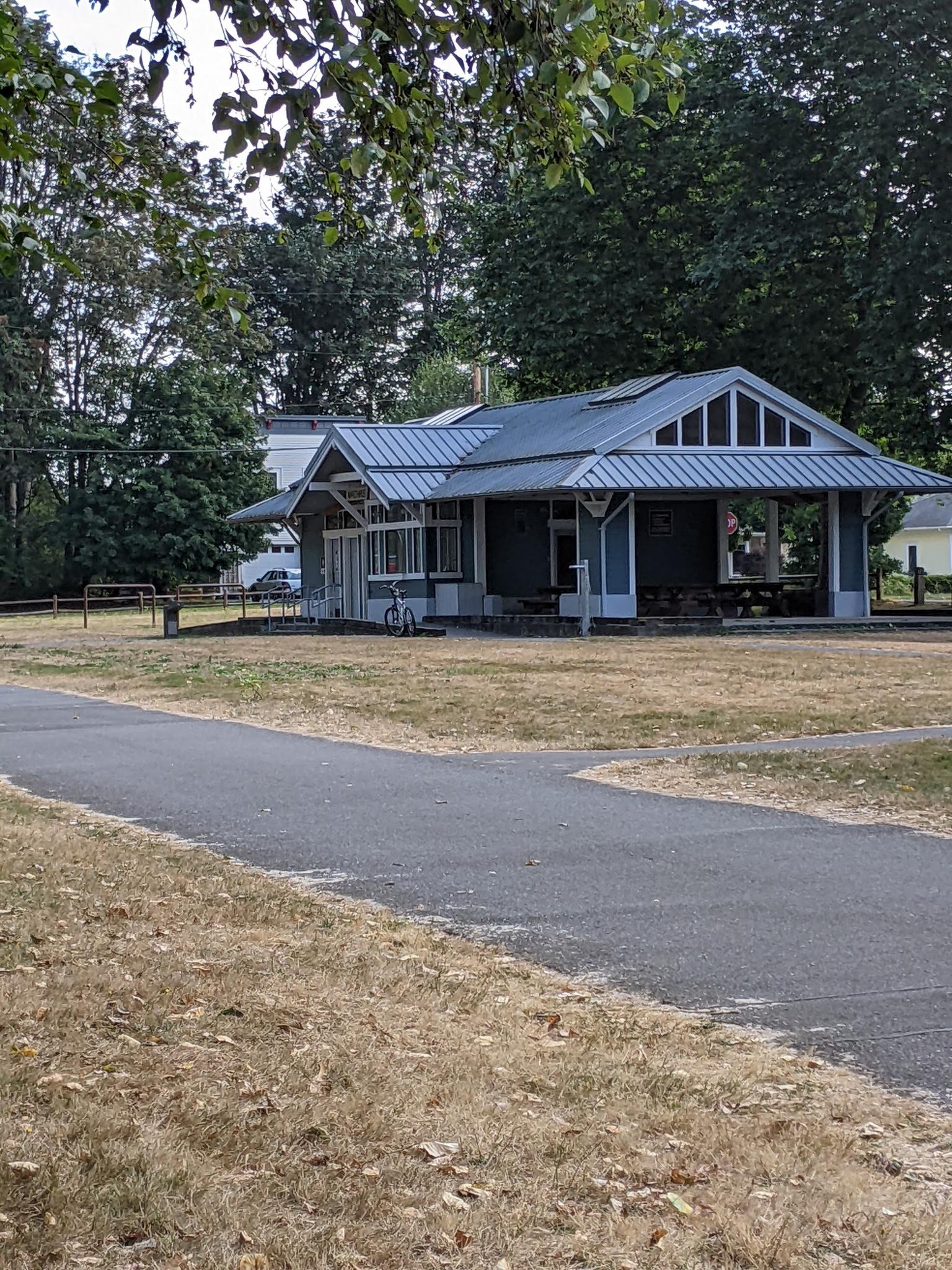 Paved path leading to a small building with a blue roof, dry grass.