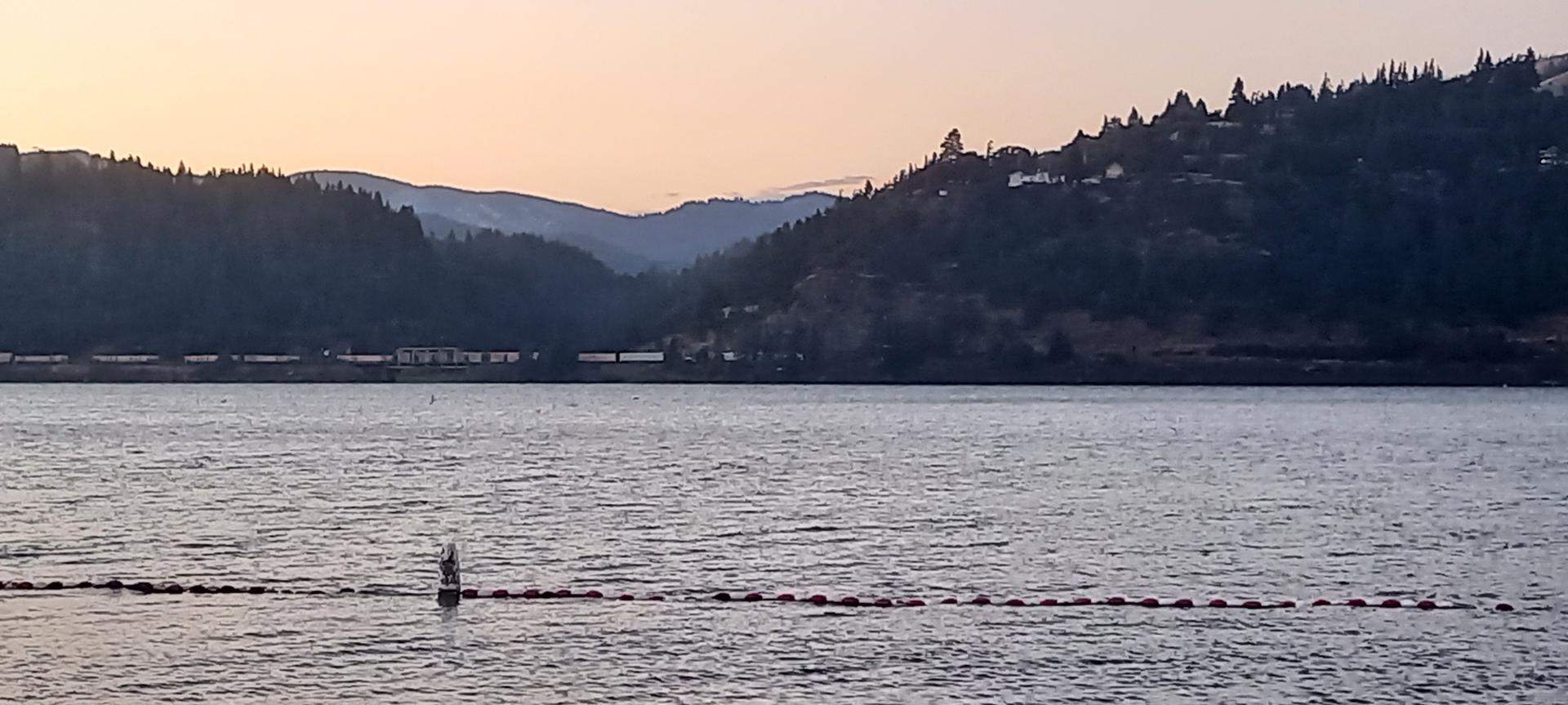 Wide body of water with buoys, distant forested hills, and soft evening light.