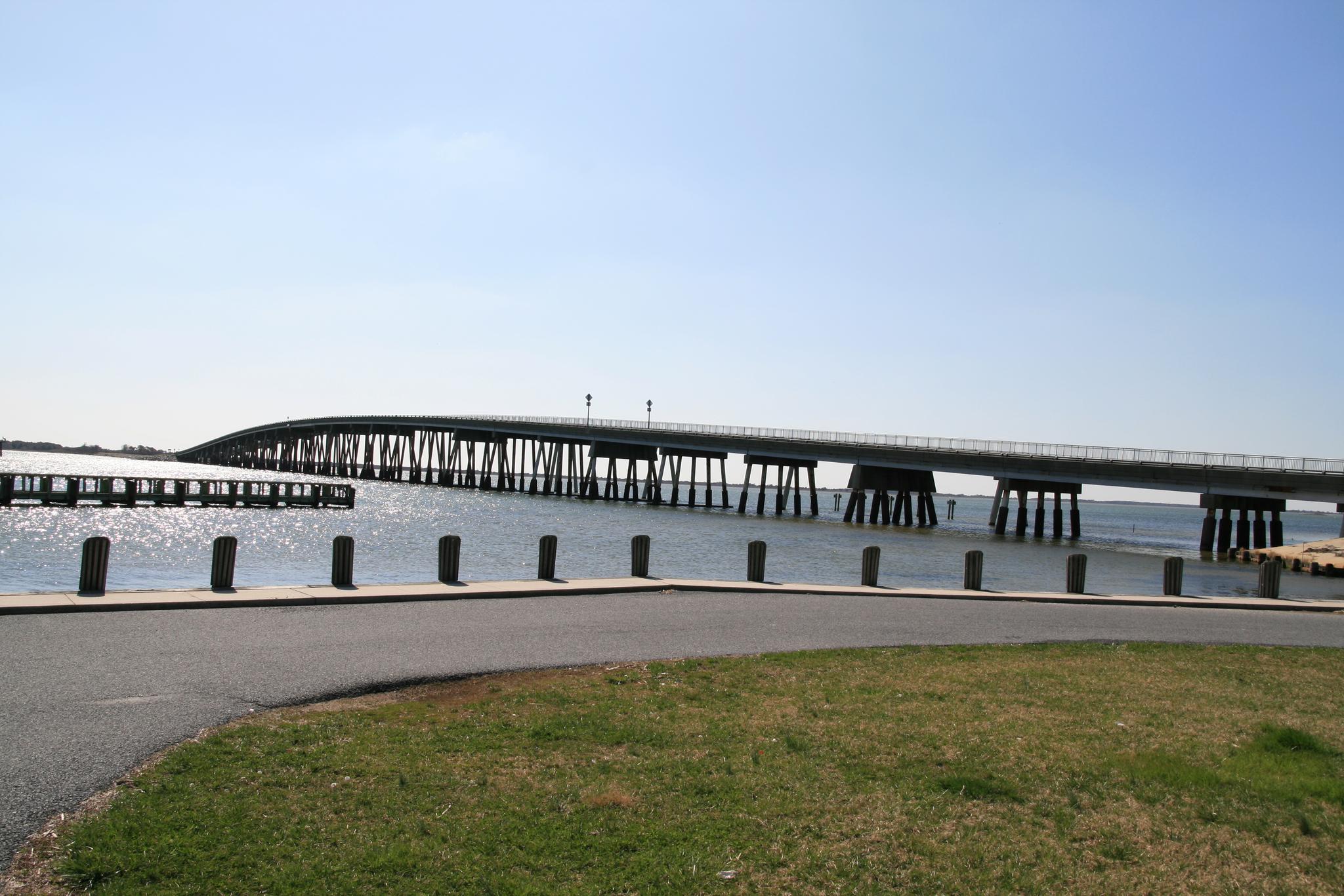 A long bridge spans calm water under a clear blue sky.