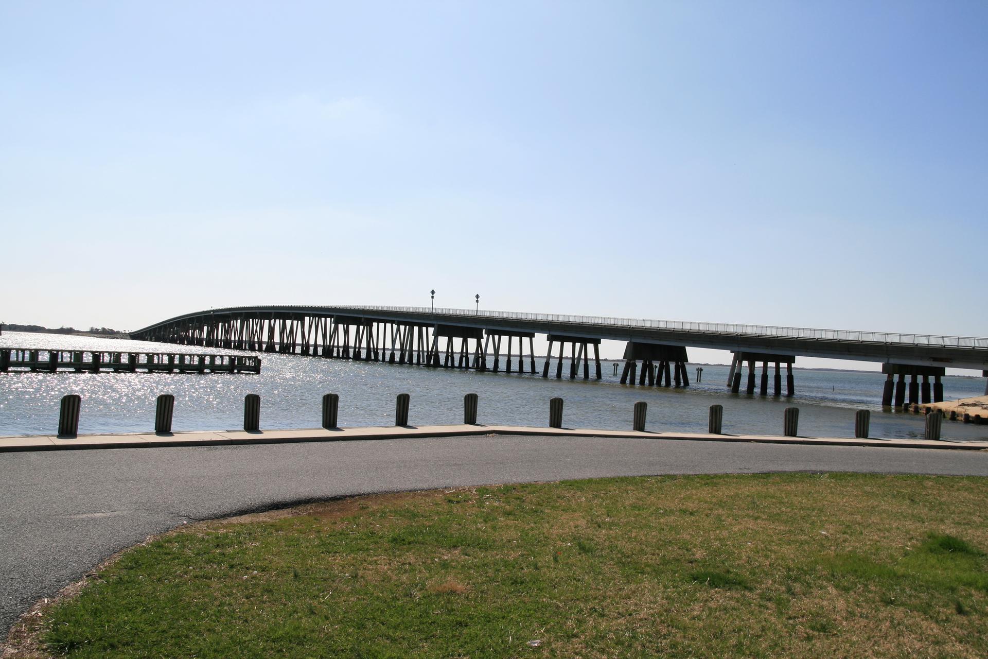 A long bridge spans calm water under a clear blue sky.