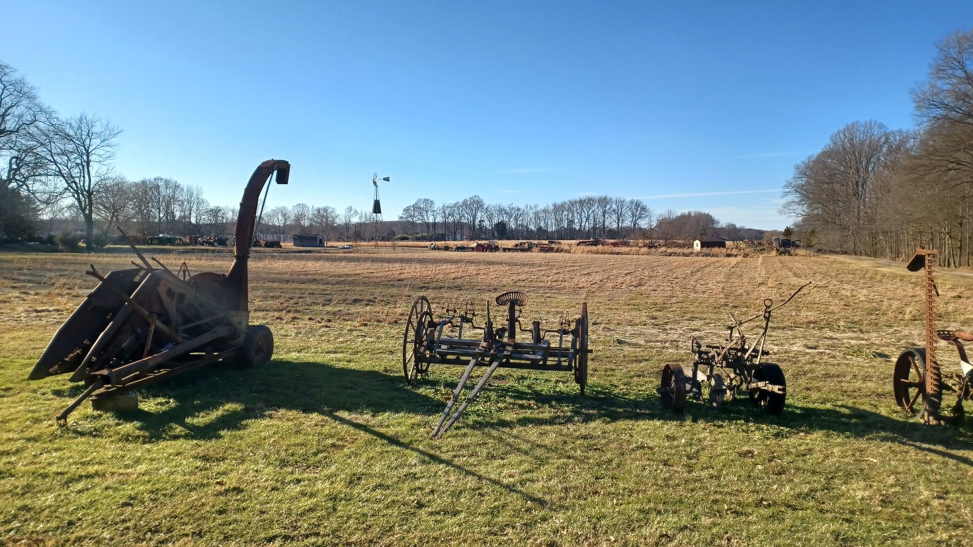 Old farm machinery sits in a sunny, grassy field with distant trees.