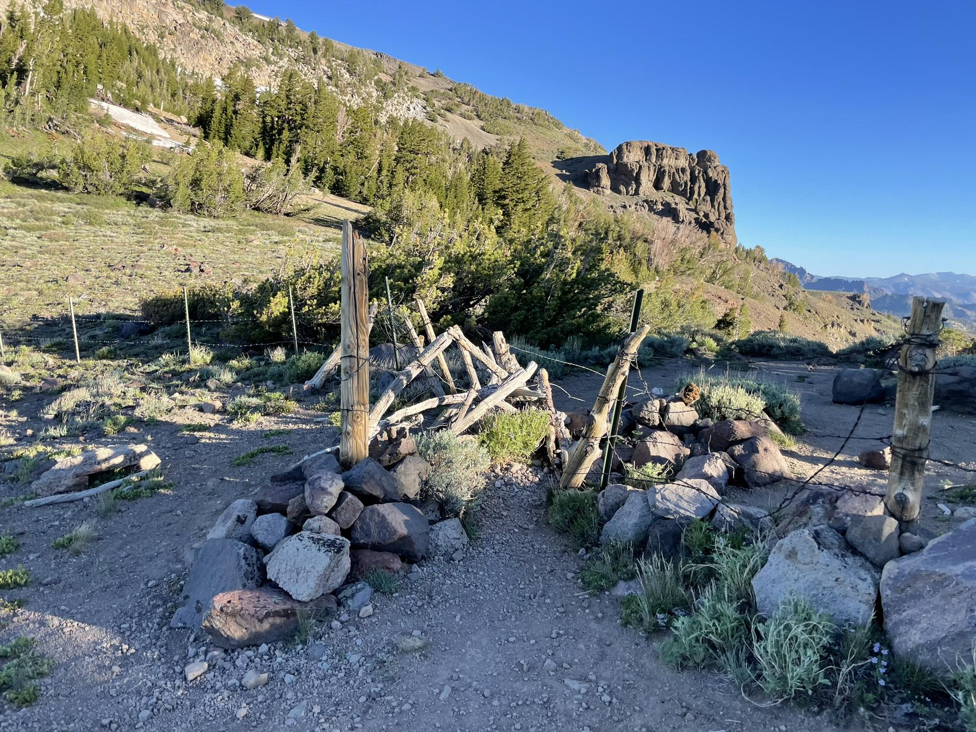 Rustic wooden gate on a rocky mountain path under bright sunlight.