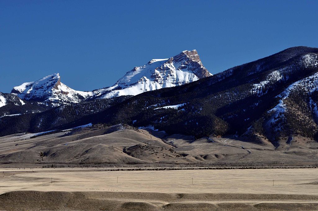 Majestic snow-capped mountains overlook a wide, dry field under a clear blue sky. - Sphinx Mountain Trail