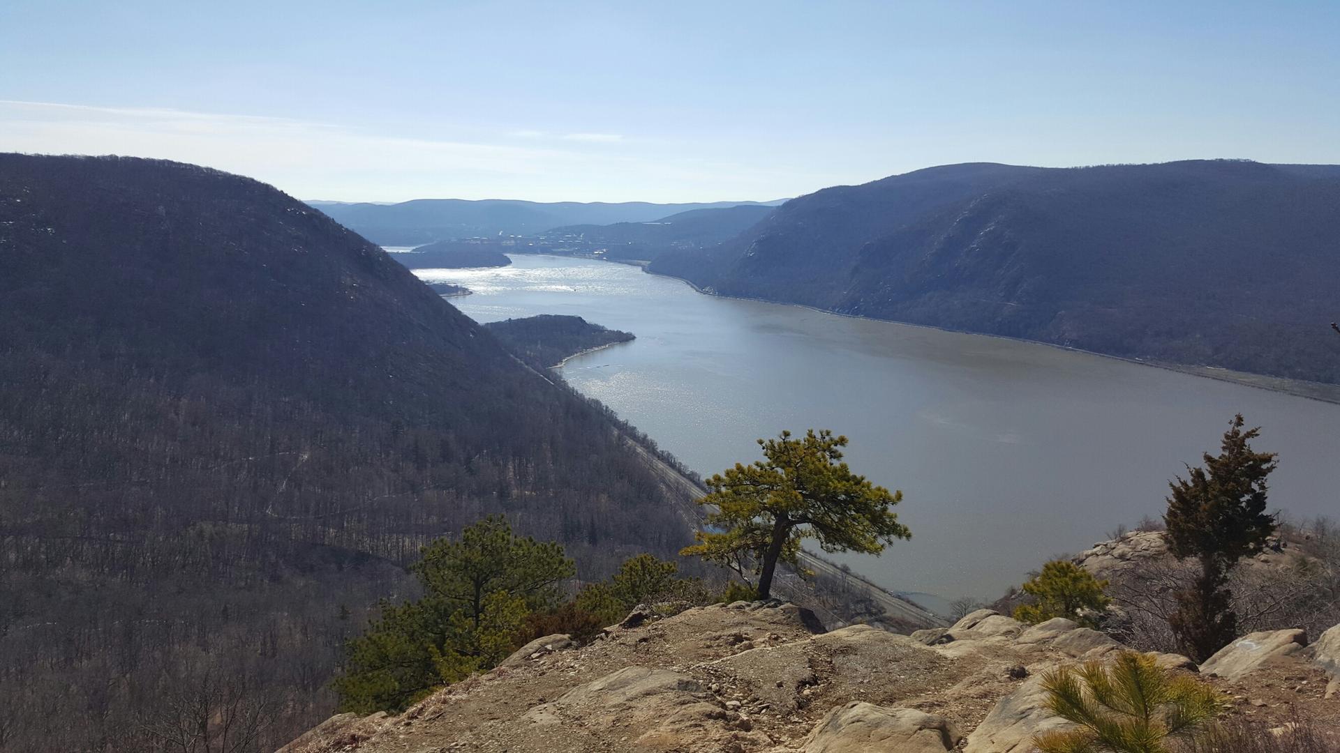 Wide river flowing between steep, forested mountains on a clear day.