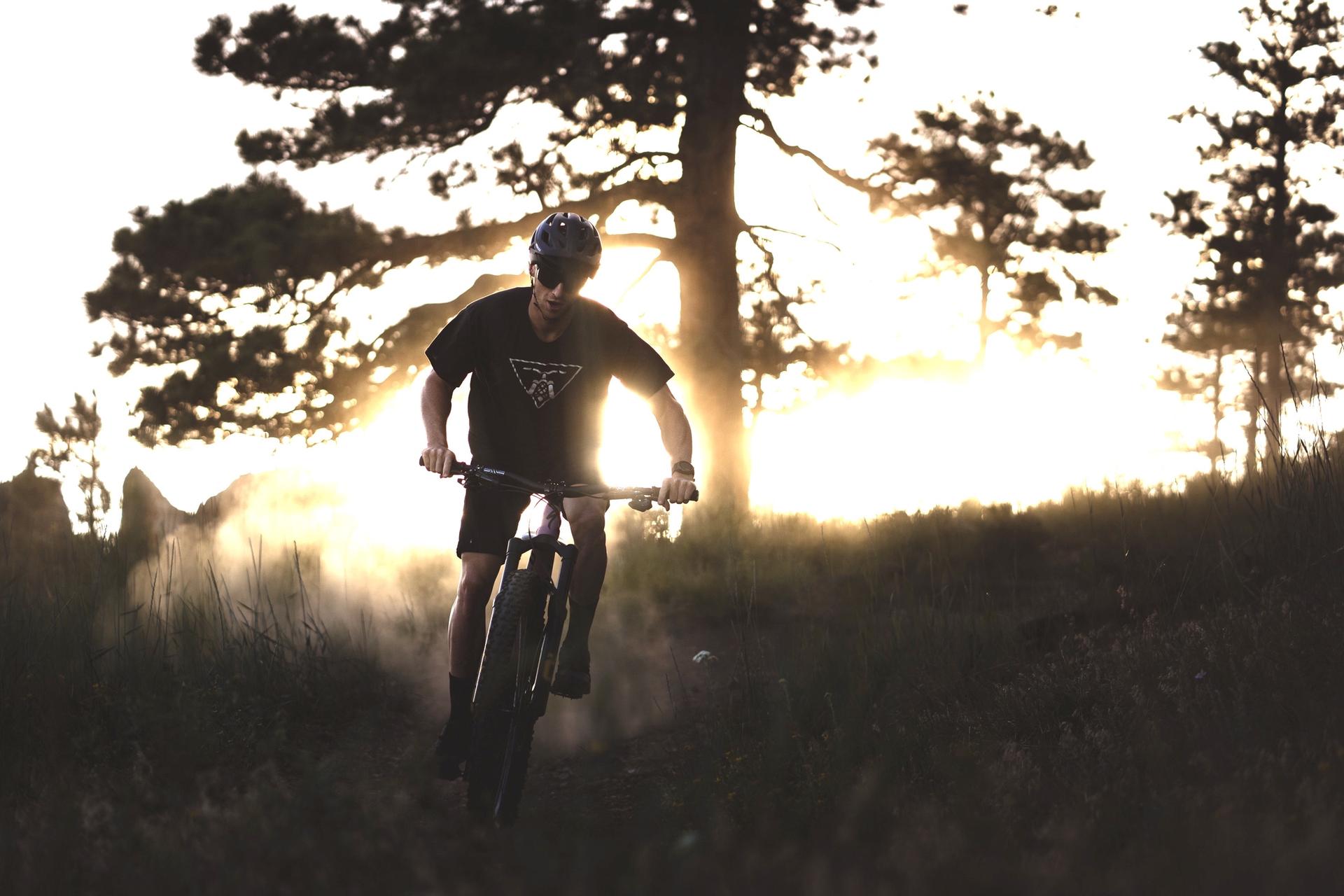 Silhouetted mountain biker rides a dusty trail during a bright sunset.