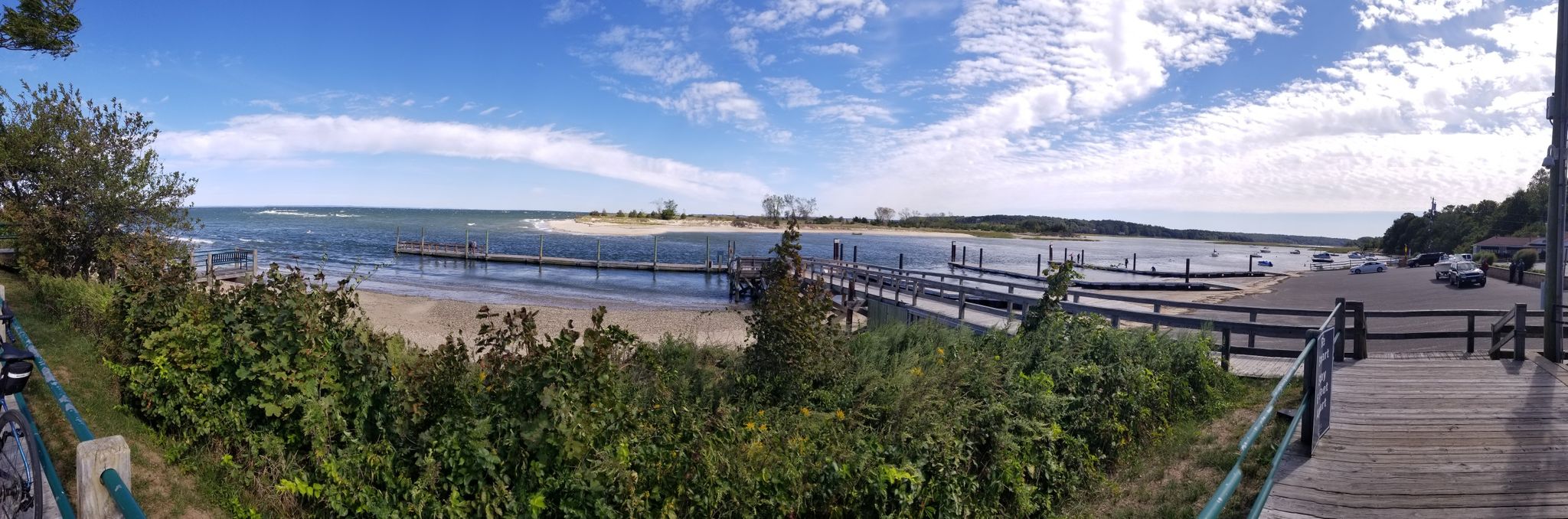 Panoramic view of a bay with multiple docks, a sandy beach, and blue sky. - Nissequogue River Loop