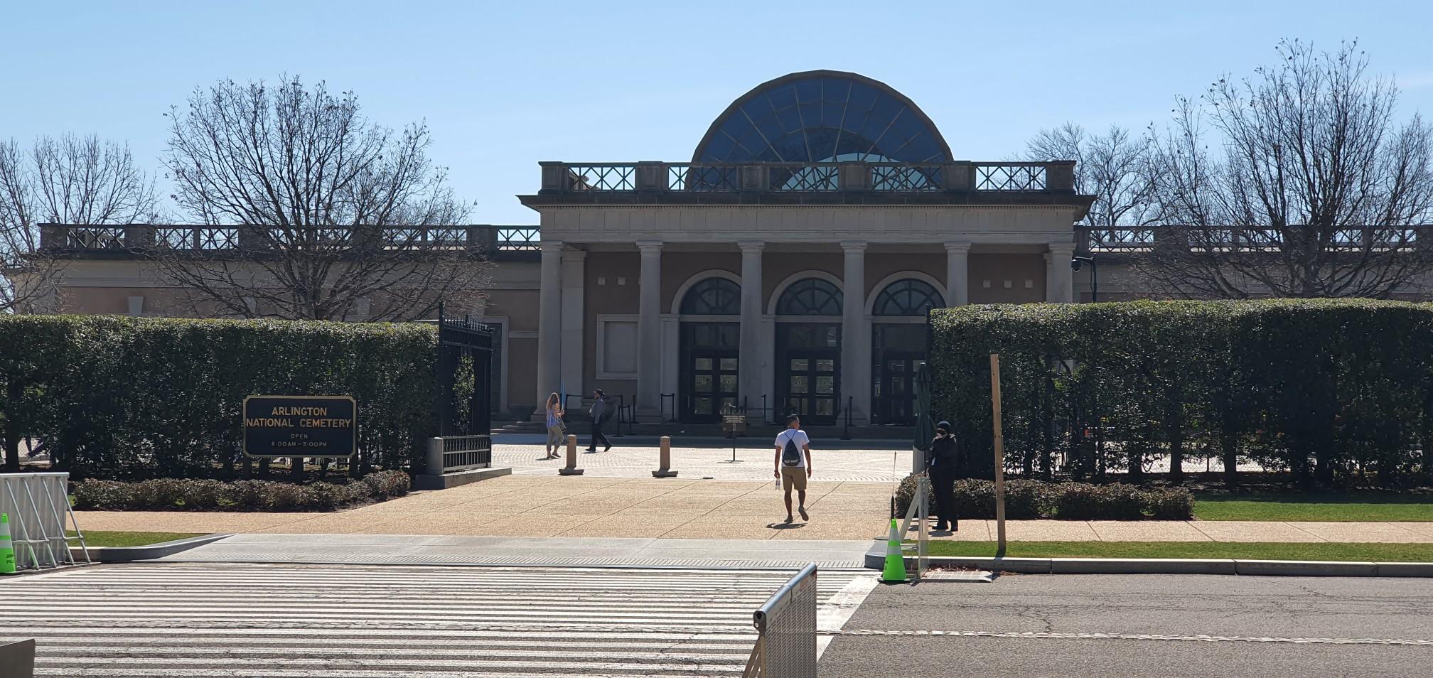 Large classical building with a domed roof and people walking in front.