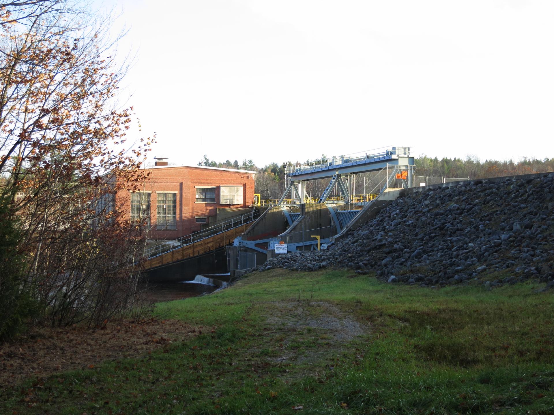 A brick building and dam with sluice gates next to a rocky embankment.