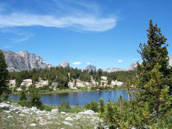 A serene mountain lake surrounded by pine trees and distant peaks.