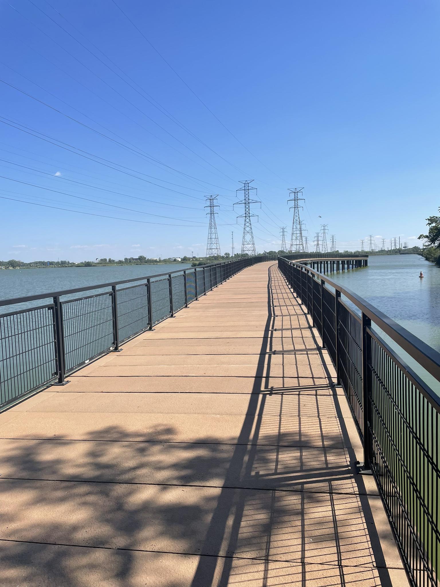 Long wooden boardwalk over water under a clear, sunny sky.