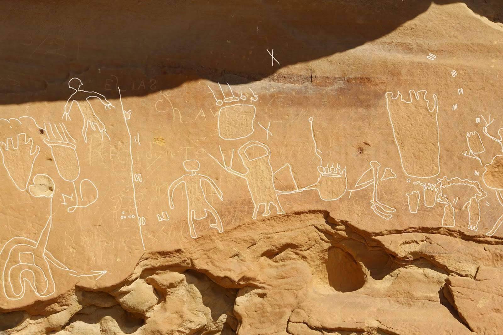 Ancient petroglyphs depicting figures carved into a sunlit rock.