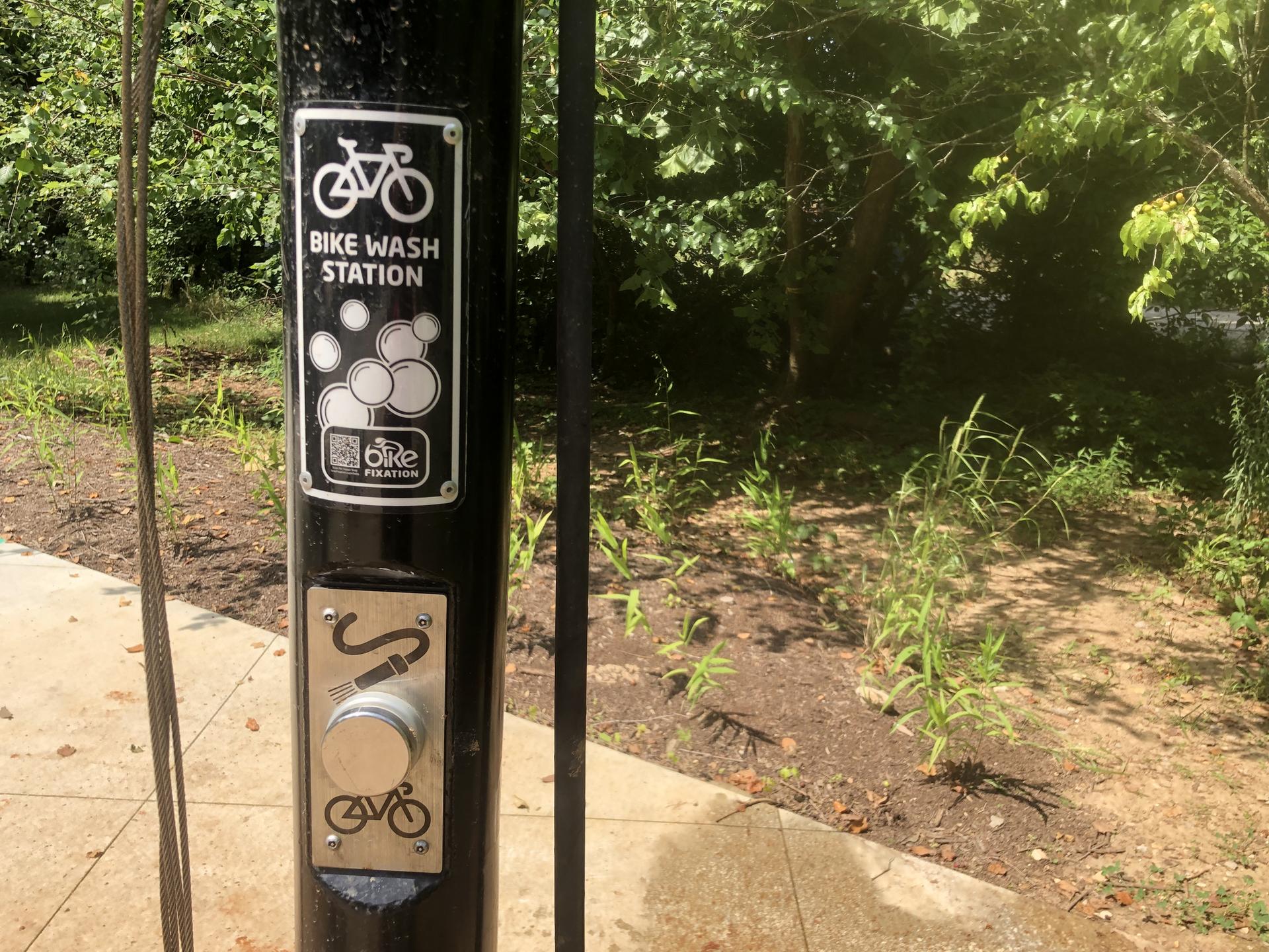A bike wash station sign and pump on a black pole, with green foliage.
