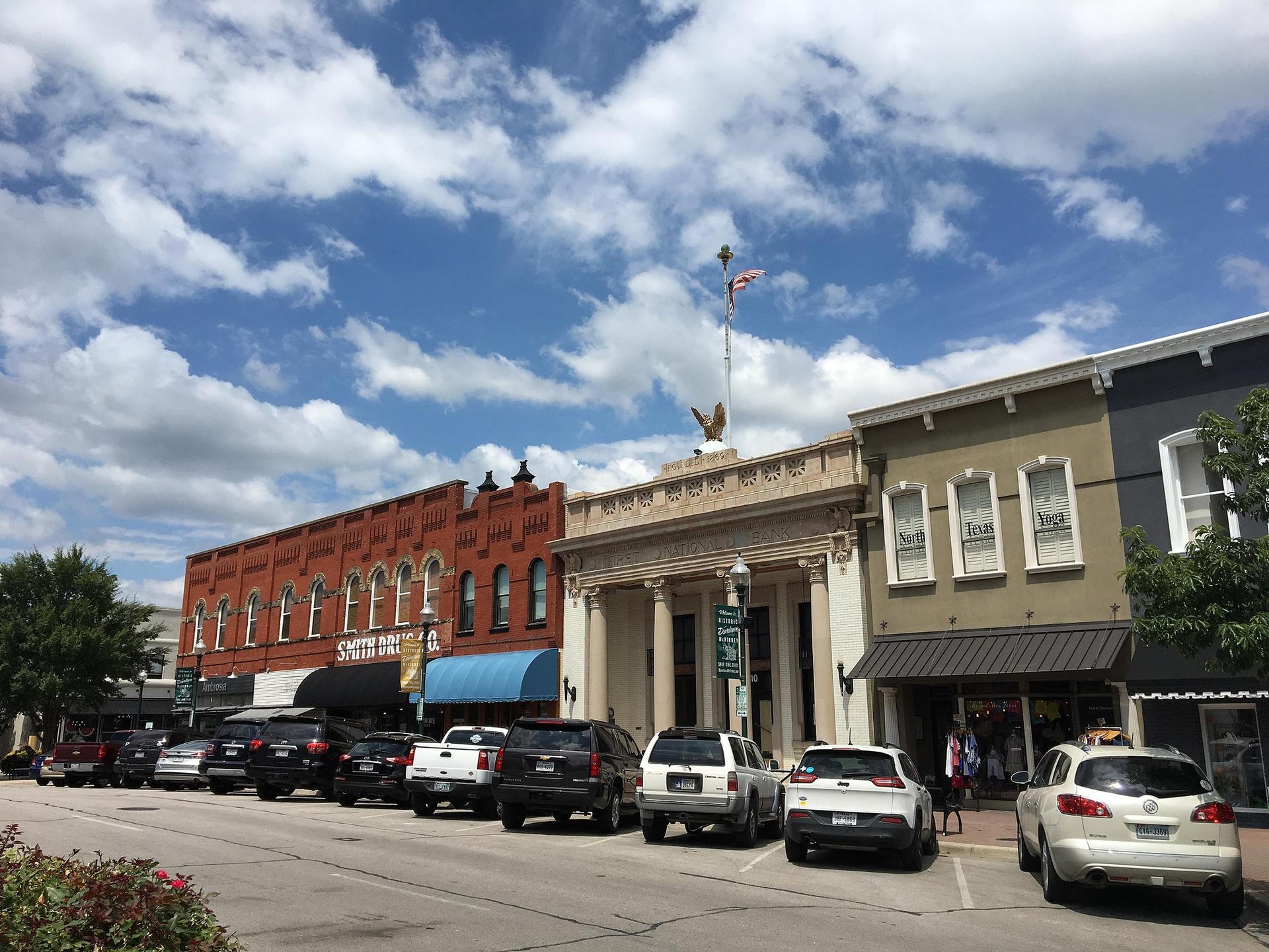 Street lined with parked cars and historic buildings under a partly cloudy sky.