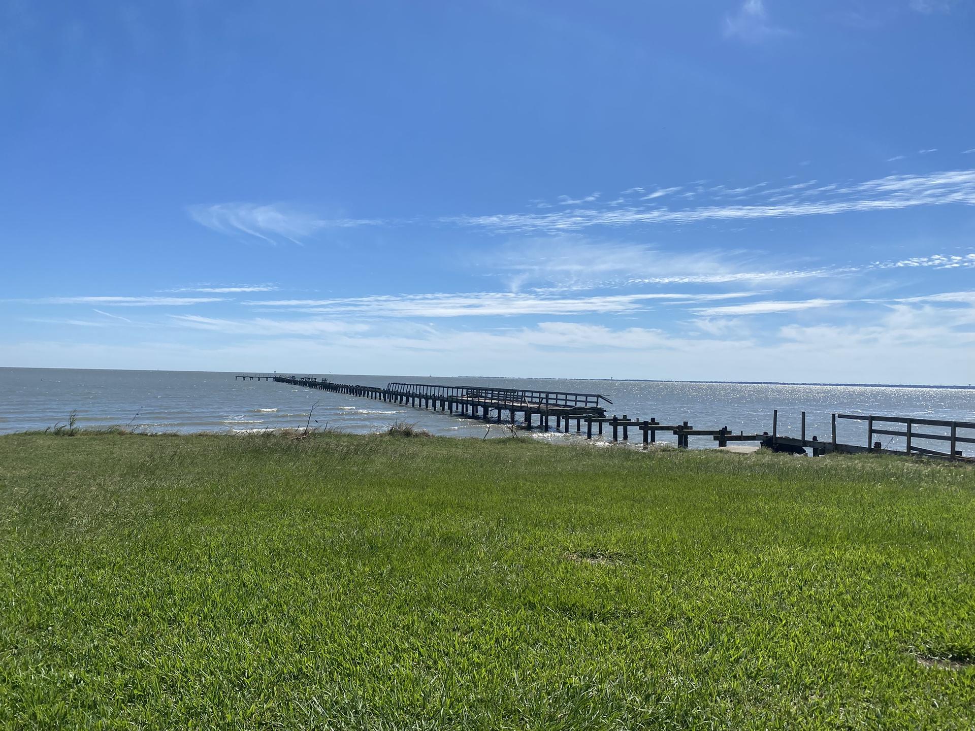 Long wooden pier extends over calm water under a bright blue sky.