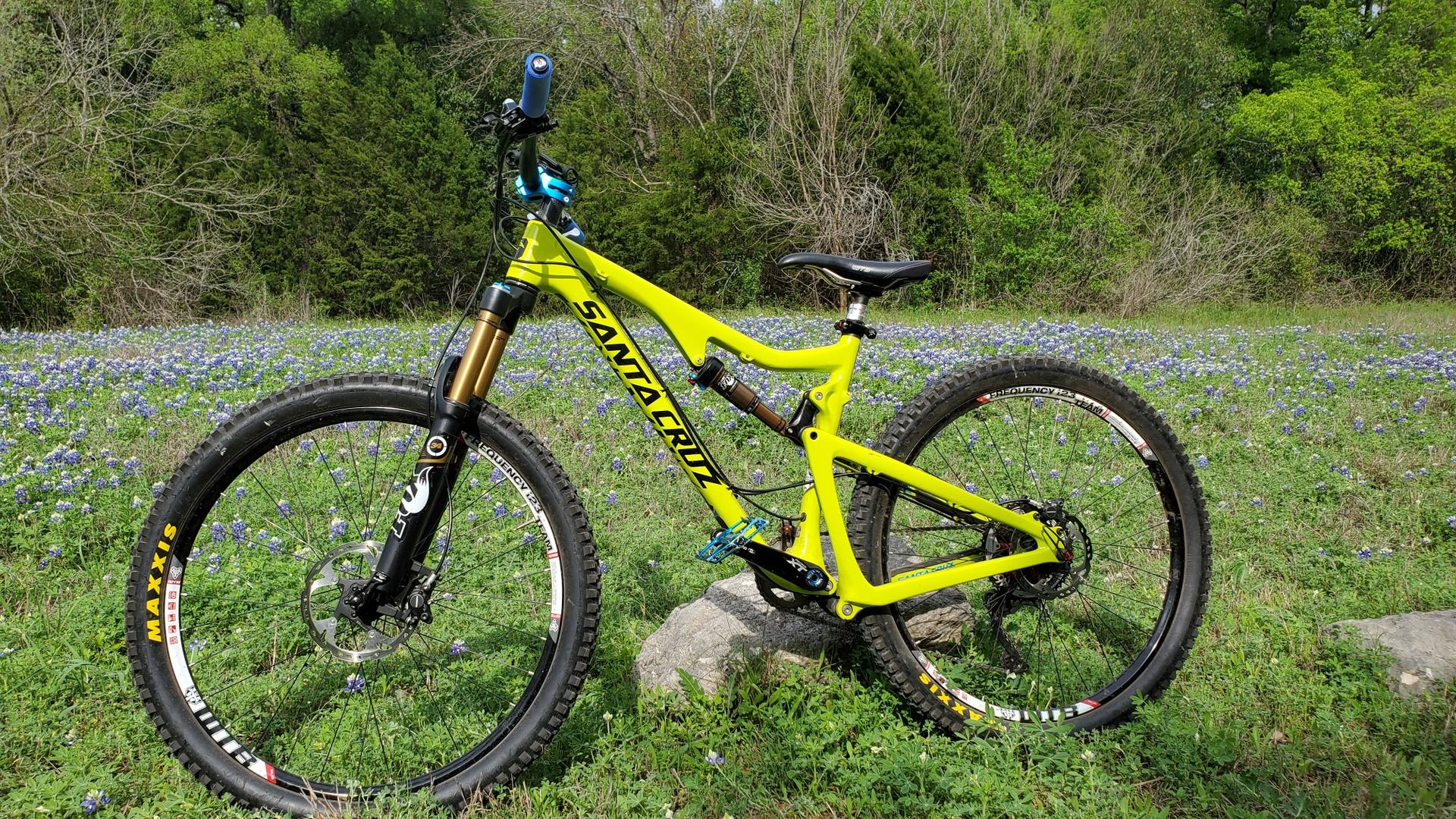 A bright yellow mountain bike stands in a grassy field with green foliage.