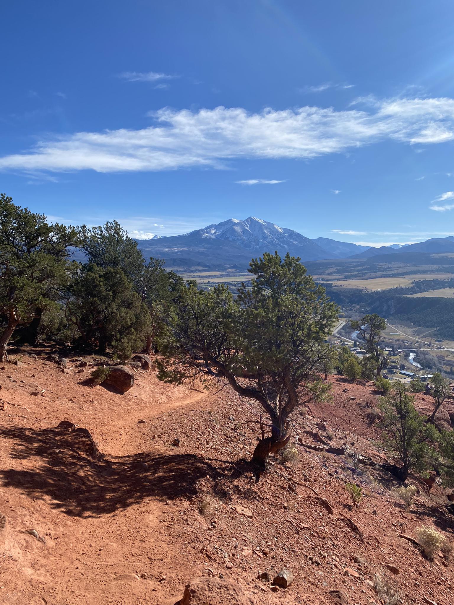 Scenic mountain view from a red dirt trail under a blue sky.