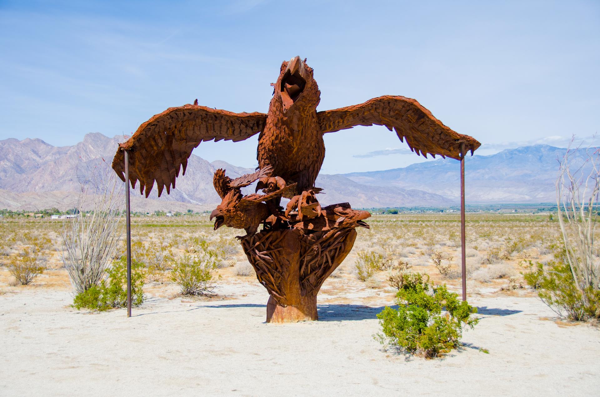 Intricate metal sculpture of an eagle and birds in a vast desert landscape.