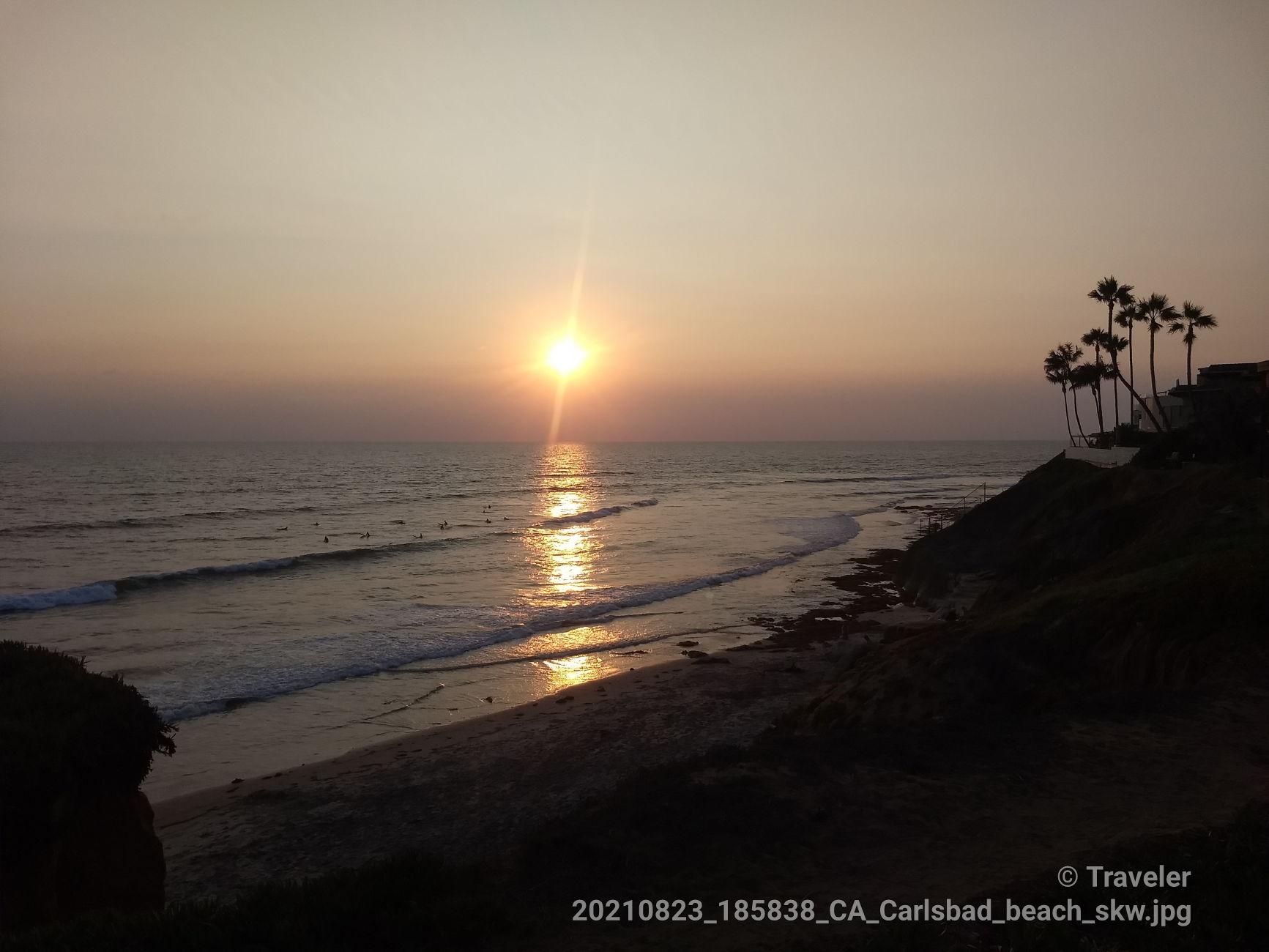 Golden sunset over the ocean, with palm trees silhouetted on a dark cliff.