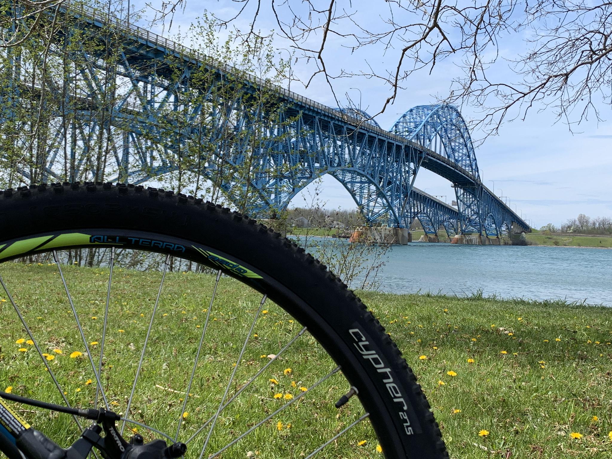 A bicycle wheel in foreground with a large blue truss bridge over water.