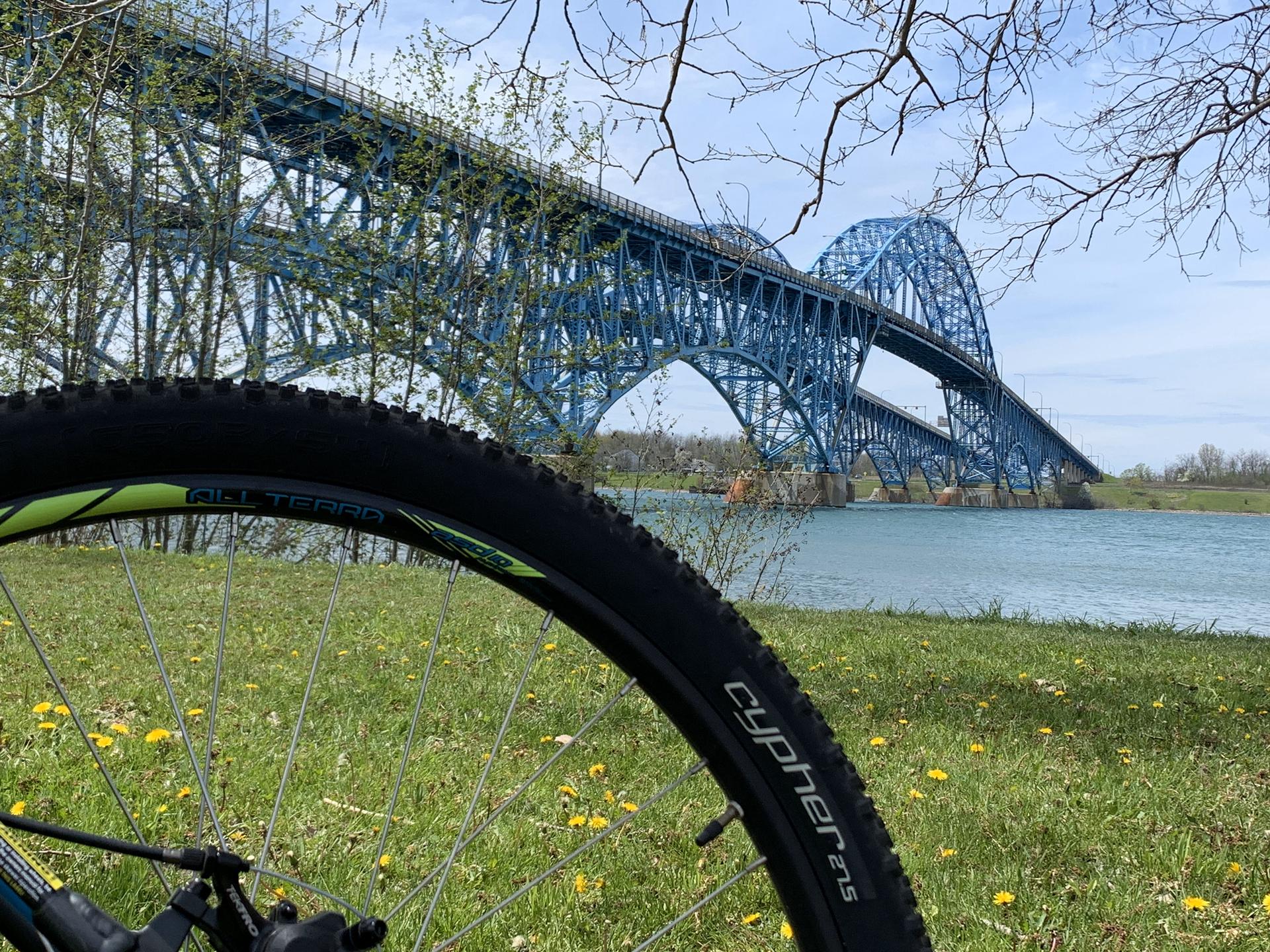 A bicycle wheel in foreground with a large blue truss bridge over water.