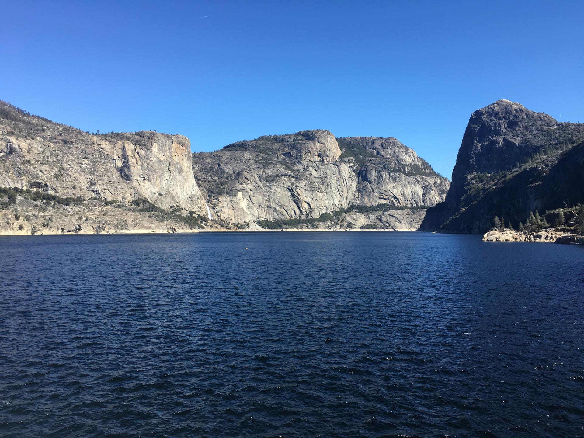 Calm, dark blue lake surrounded by massive rocky cliffs under a clear sky.