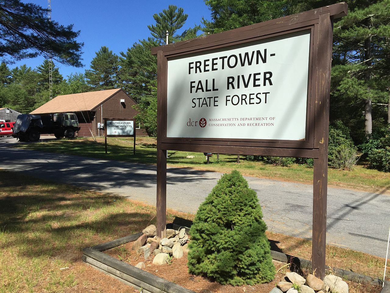 A large wooden sign, small bush, and building under bright daylight. - Freetown-Fall River State Forest – Intermediate Loop