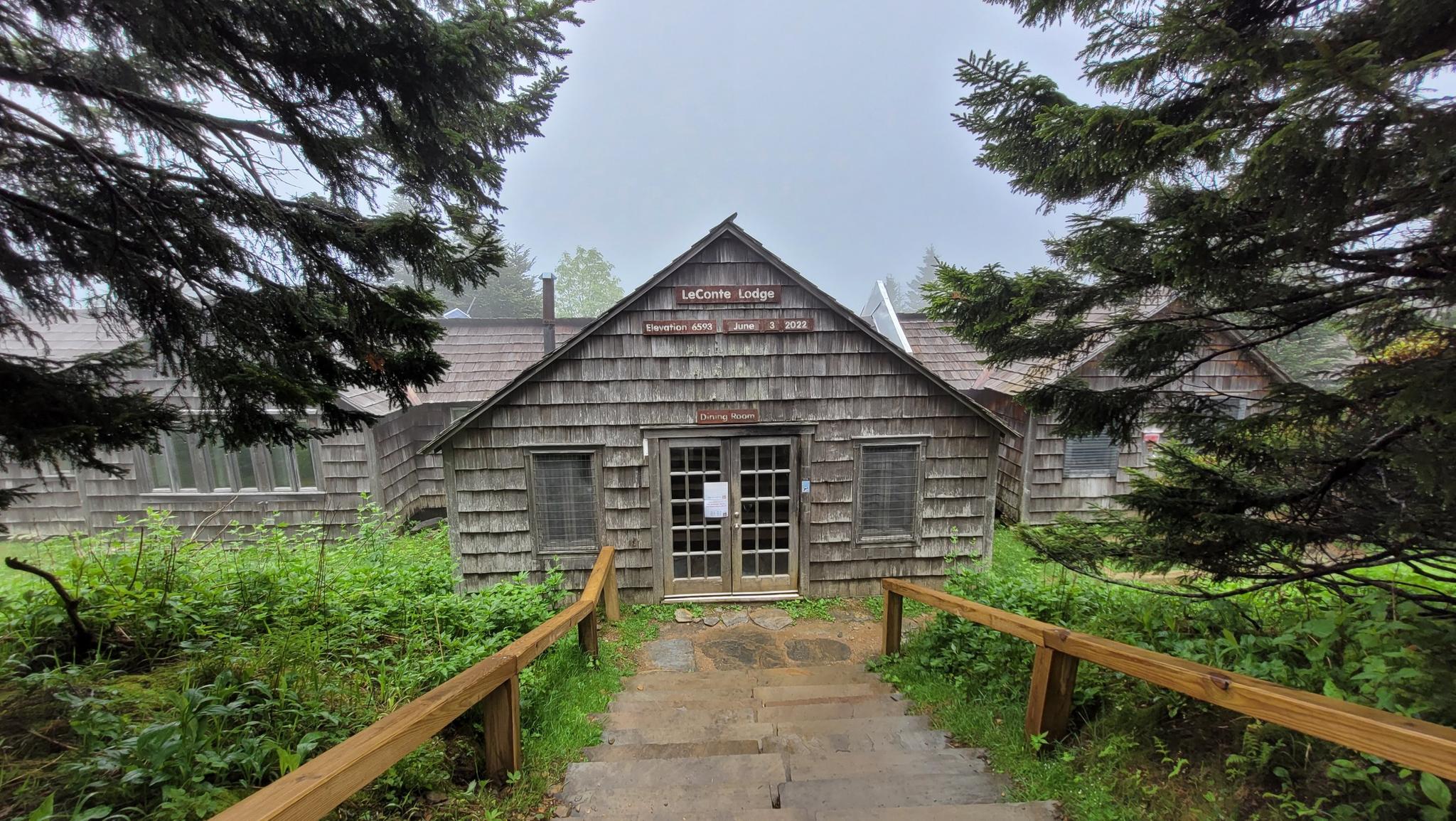 A rustic wooden lodge building on a foggy day, framed by trees.