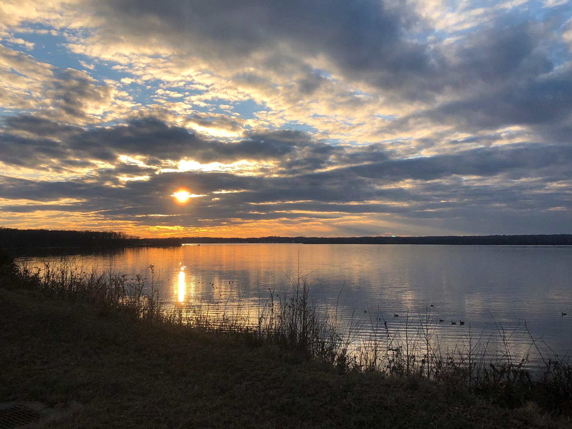 Vibrant sunset over a wide, calm lake with reflections and cloudy sky.