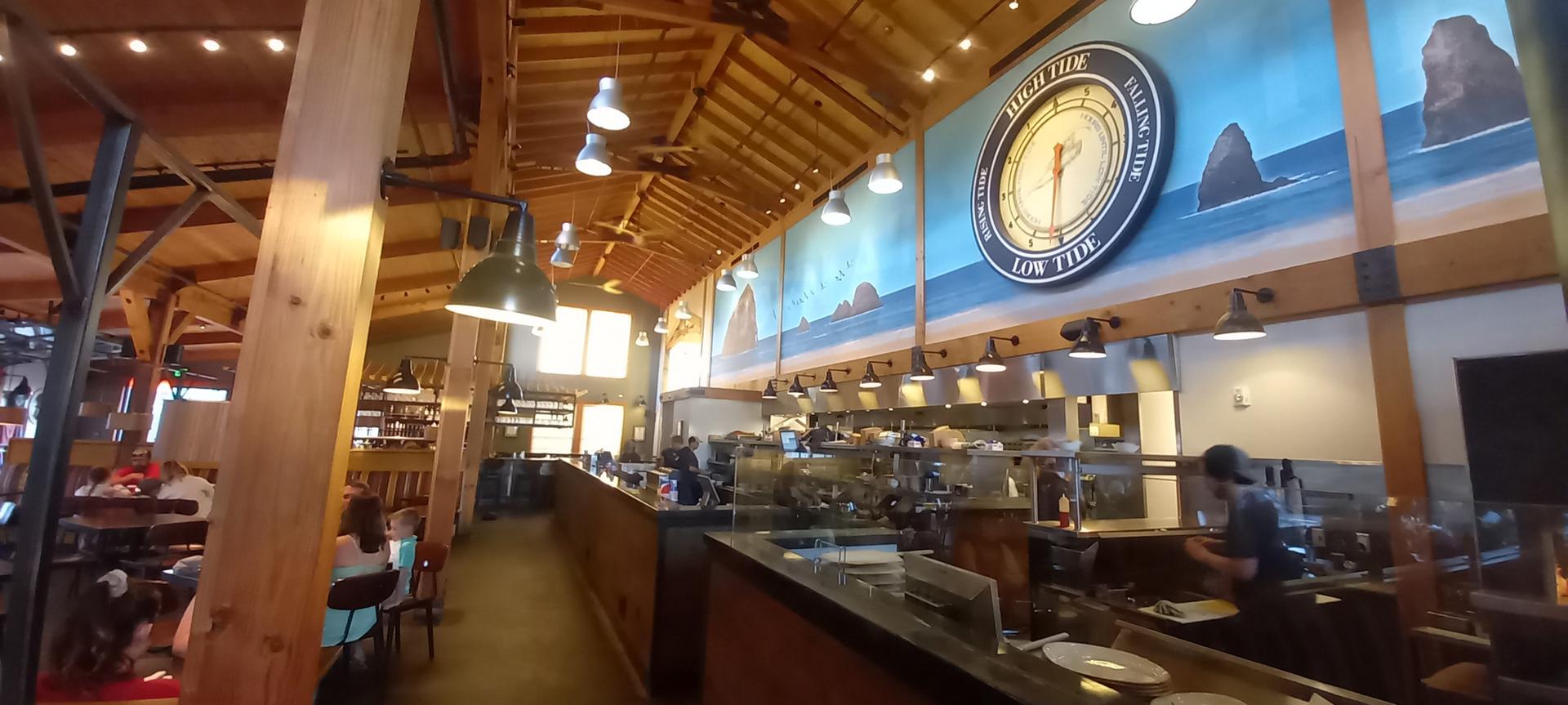 Warmly lit restaurant interior with an open kitchen, wooden beams, and diners.
