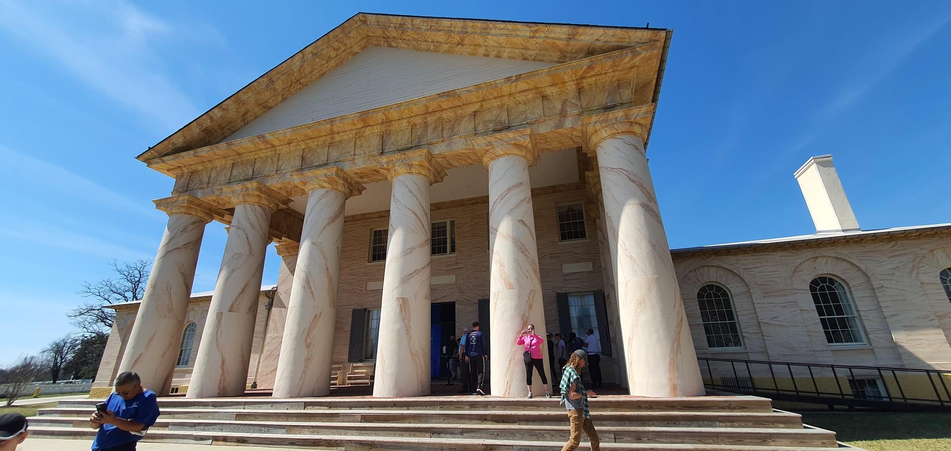Grand classical building with tall columns and steps, people entering.