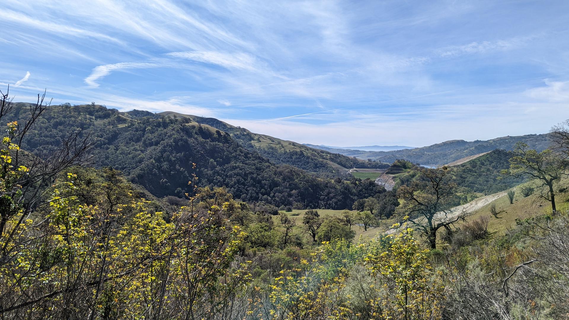 Green hills and valleys under a bright blue sky with wispy clouds.