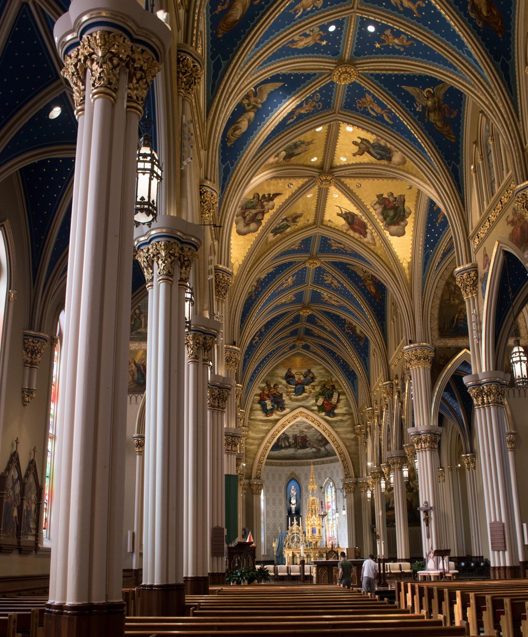 Grand church interior with ornate blue and gold vaulted ceilings and tall columns.